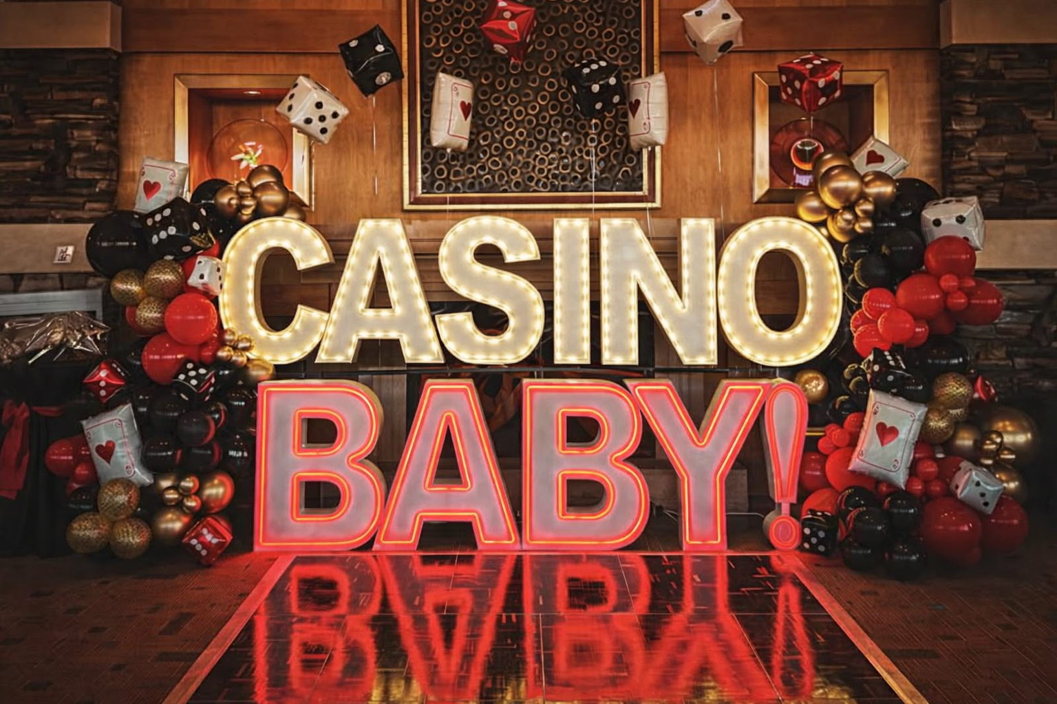 Casino Baby party decorations with lit-up letters, balloons in red, black, and gold, and playing card accents.