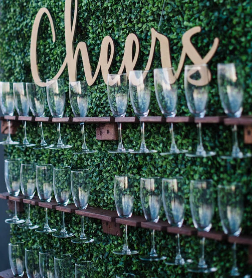 a wall of wine glasses and a sign that says cheers