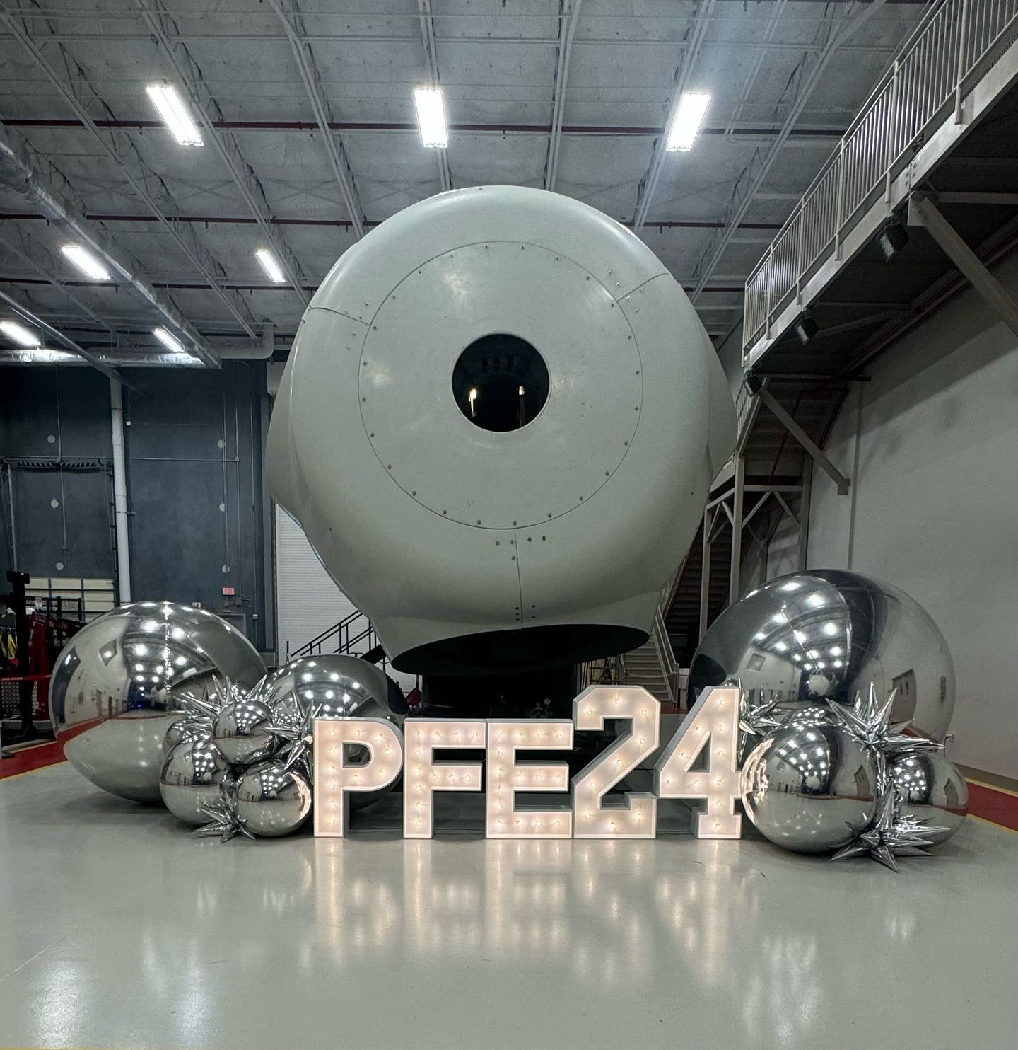 A large airplane engine is surrounded by balloons and letters that say pfe24
