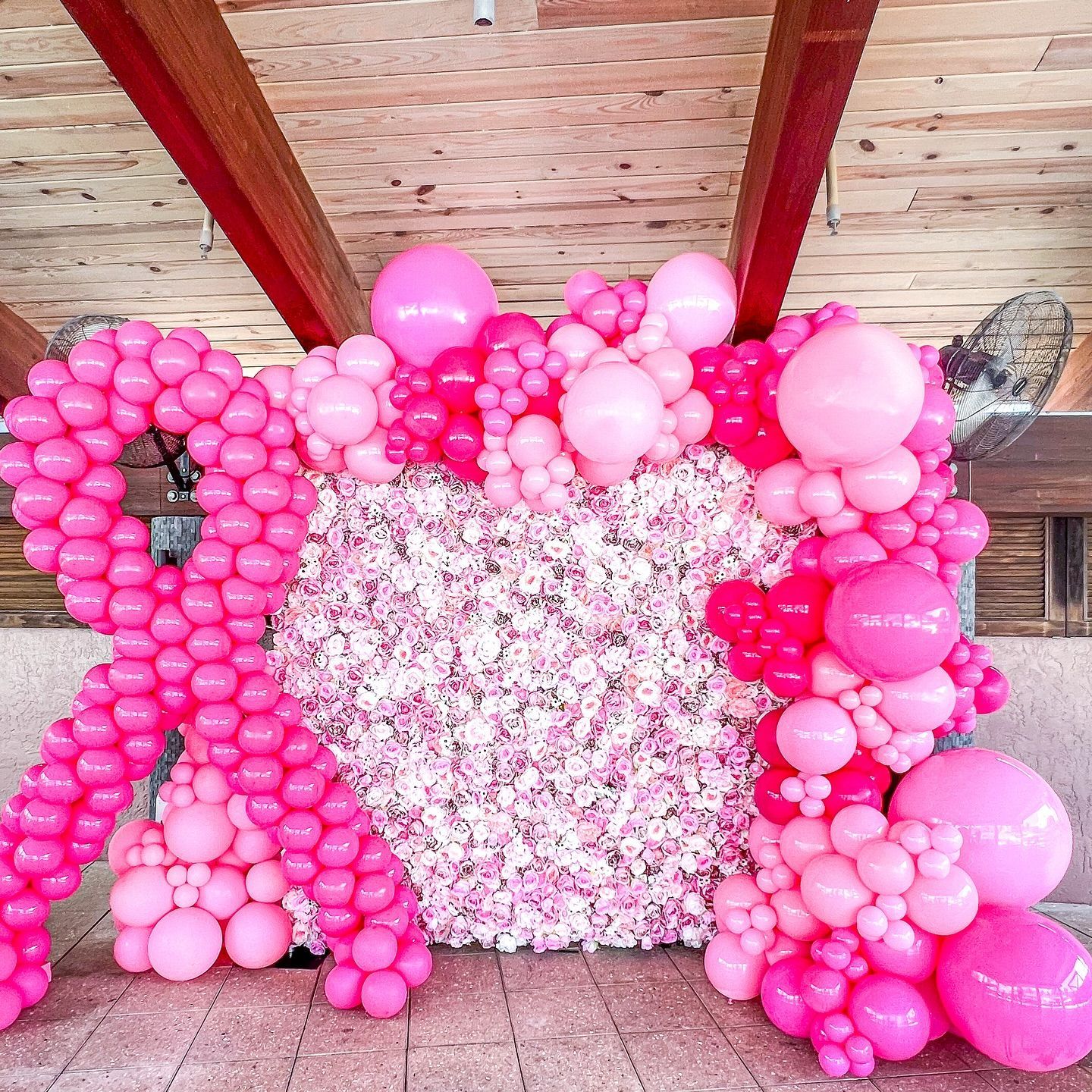 Pink breast cancer awareness ribbon made of balloons, with a floral wall.