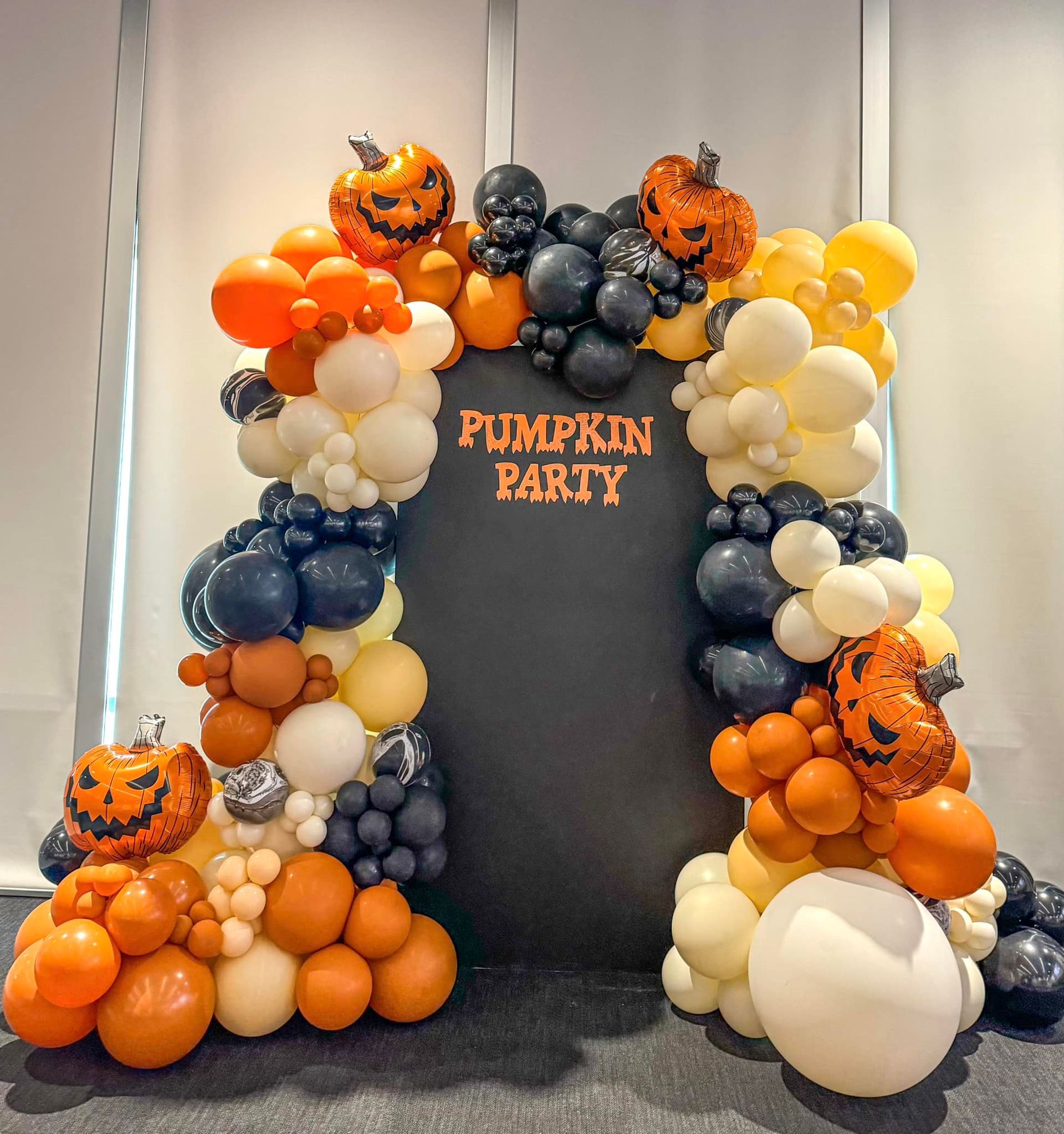 Halloween balloon arch with pumpkins, black backdrop says