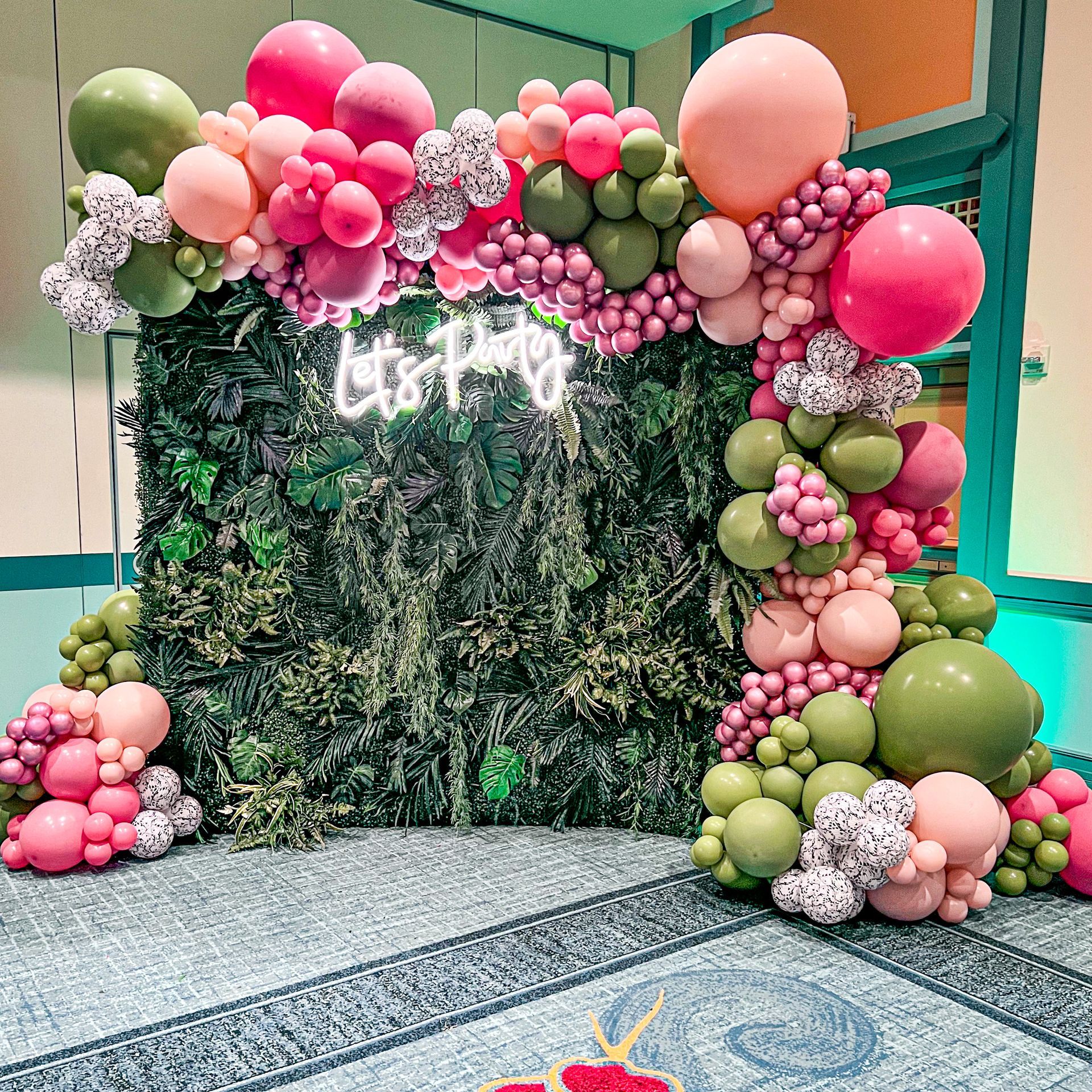 A wall covered in pink and green balloons and a neon sign.