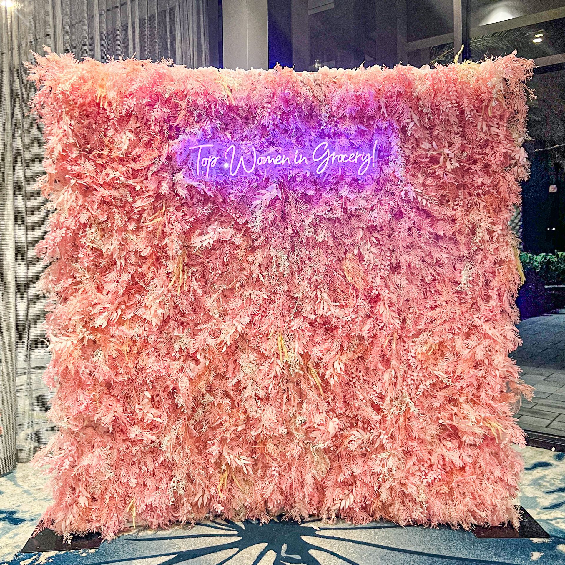 a pink flower wall with a neon sign behind it .