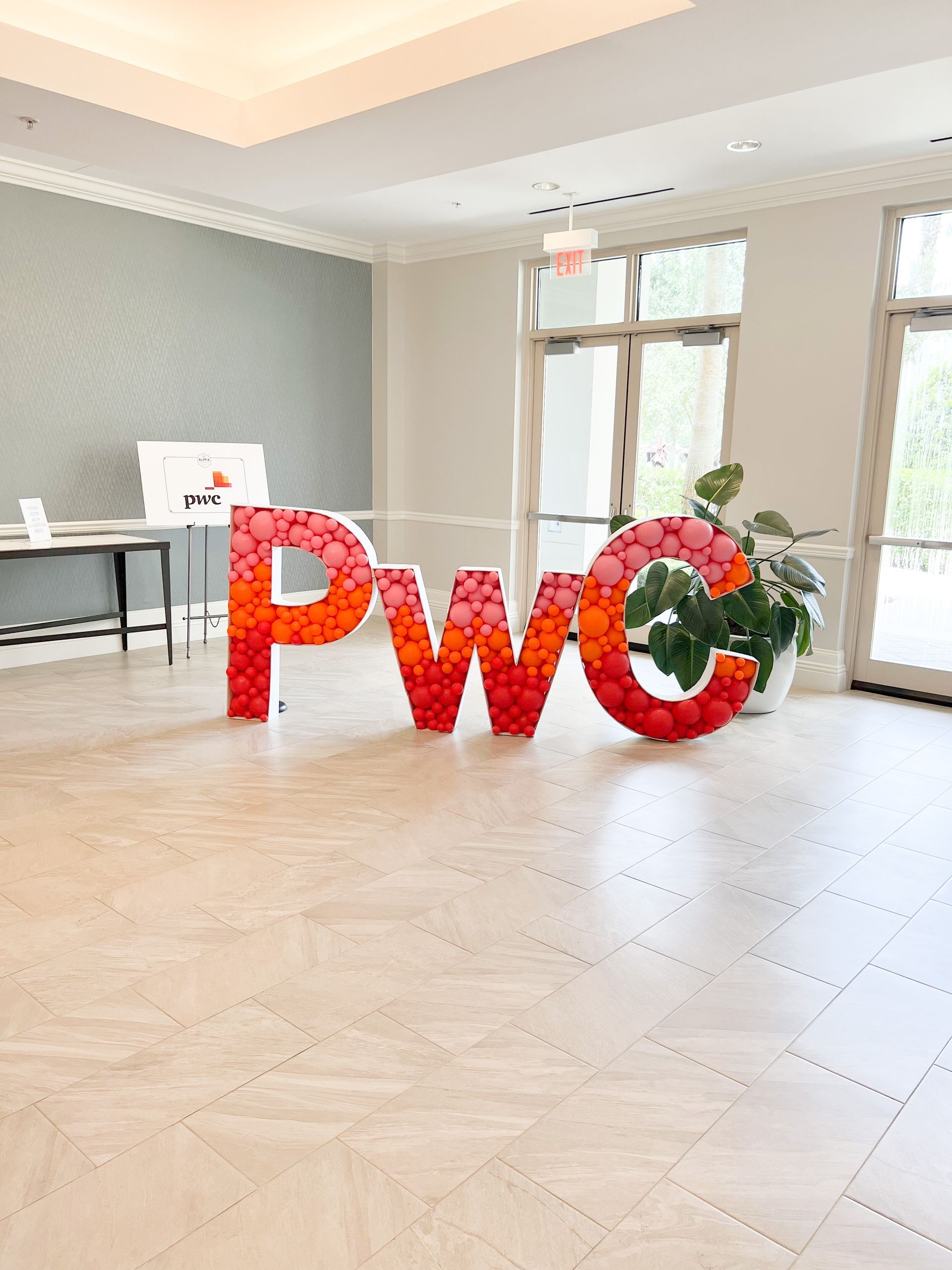 The word pwc is made of red balloons in a room.