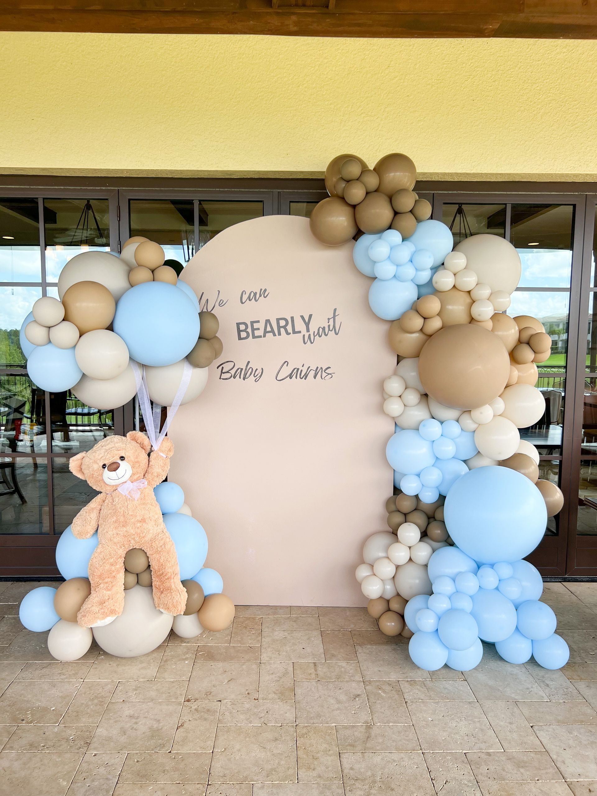 a teddy bear is standing in front of a wall covered in balloons .