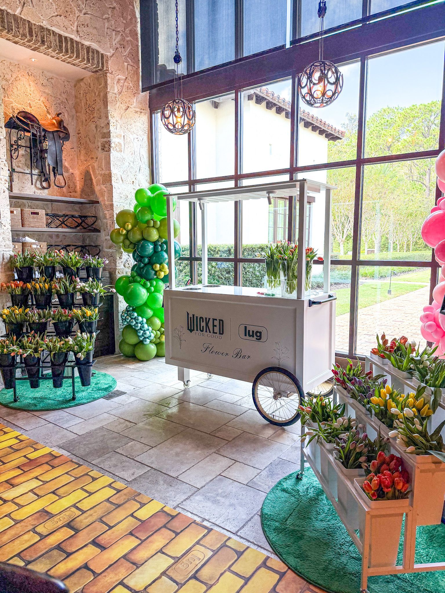 Flower cart and displays with green and yellow balloons in a brightly lit room.