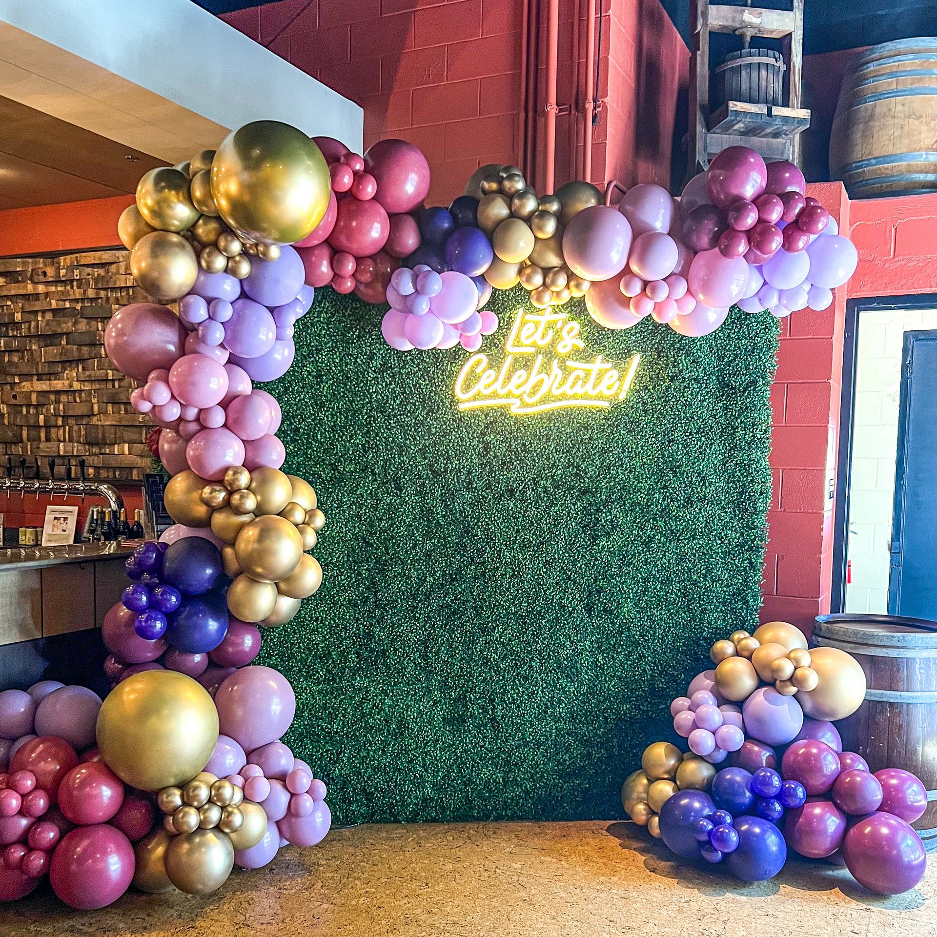 a wall covered in balloons and a neon sign that says `` let 's celebrate '' .
