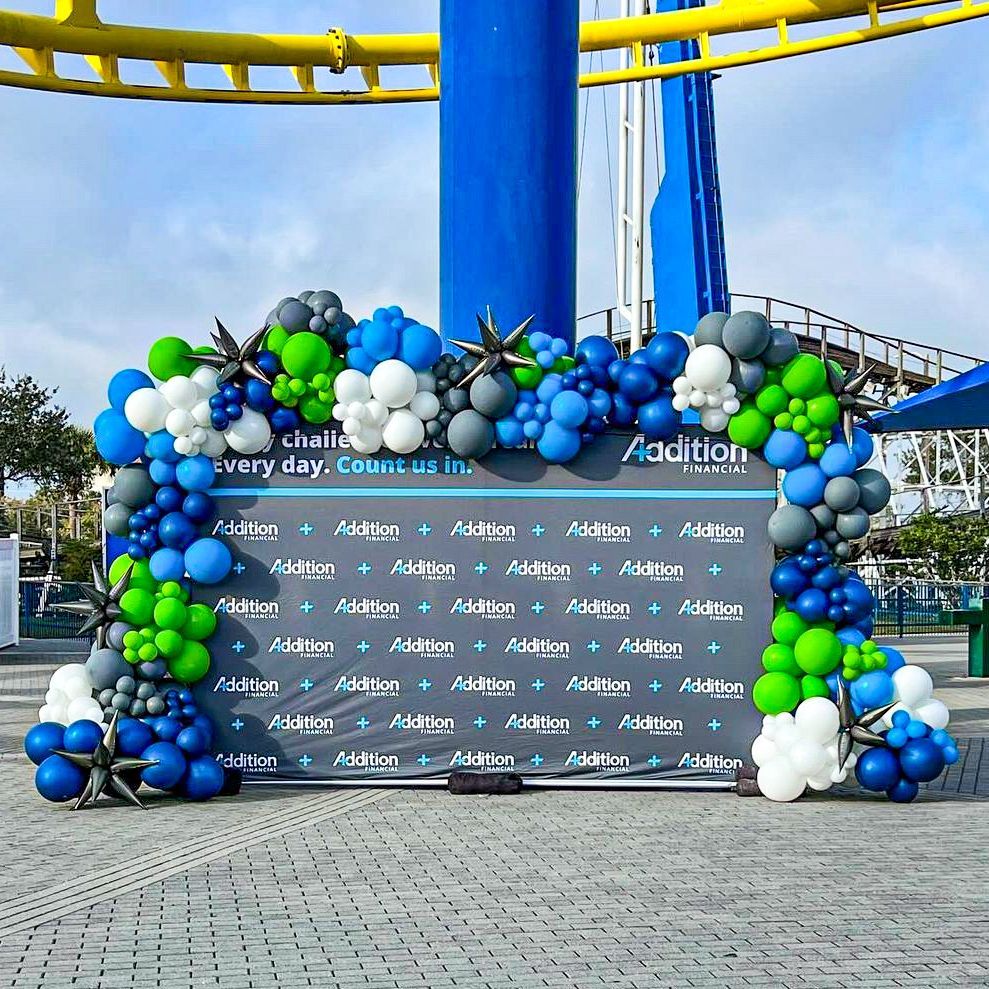 A bunch of blue and green balloons are sitting on top of a sign.