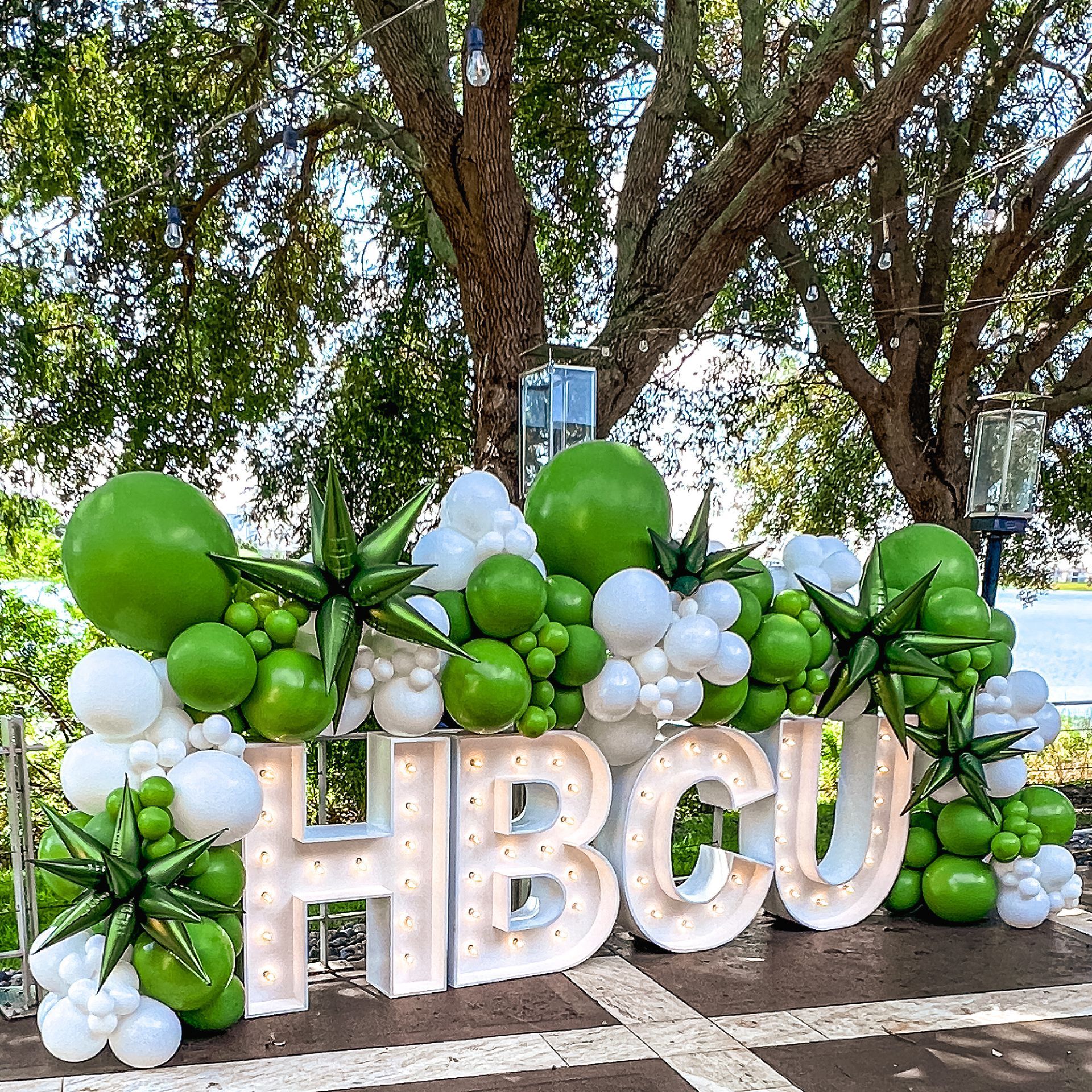 A sign that says hbcu is surrounded by green and white balloons.