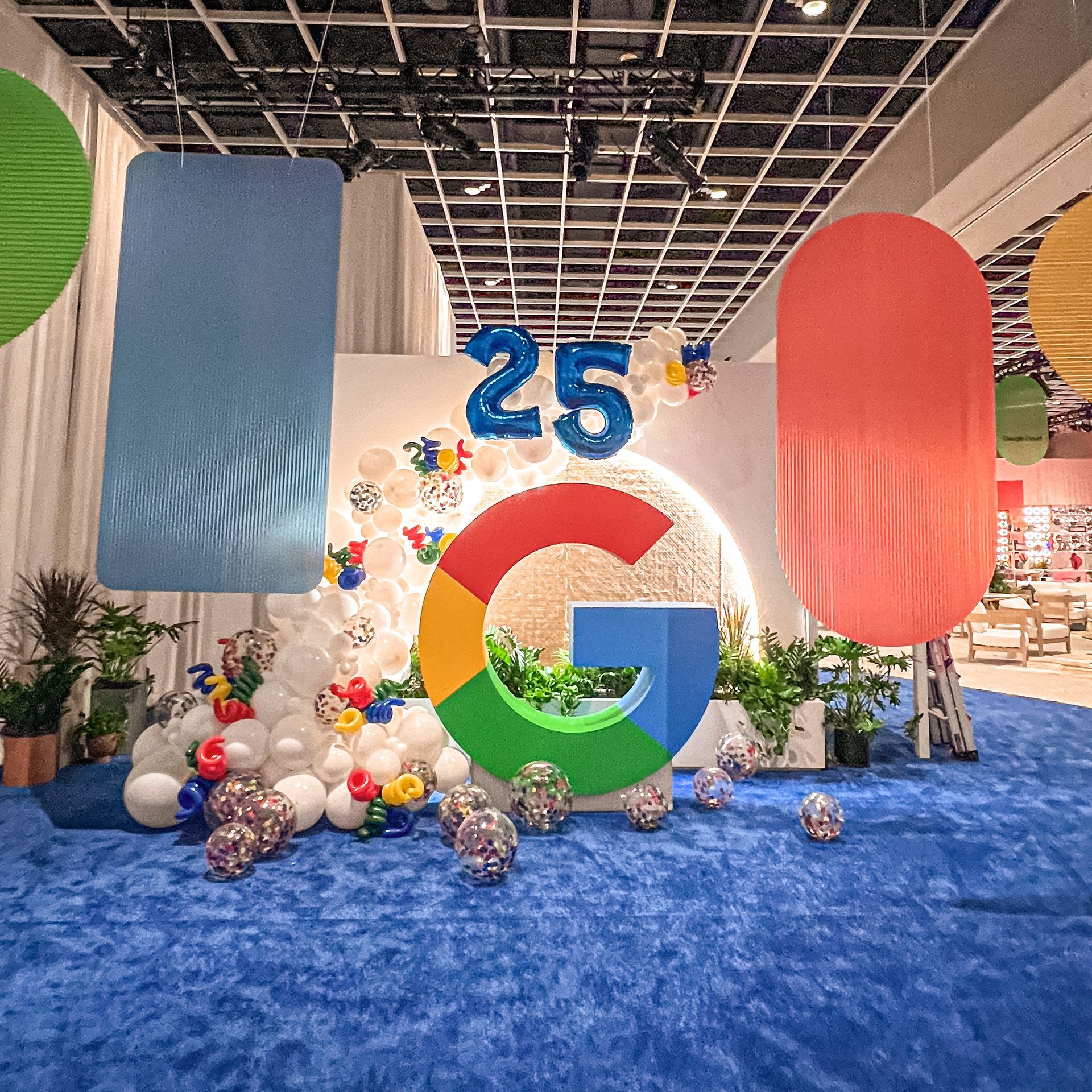 A large google logo is surrounded by balloons and plants