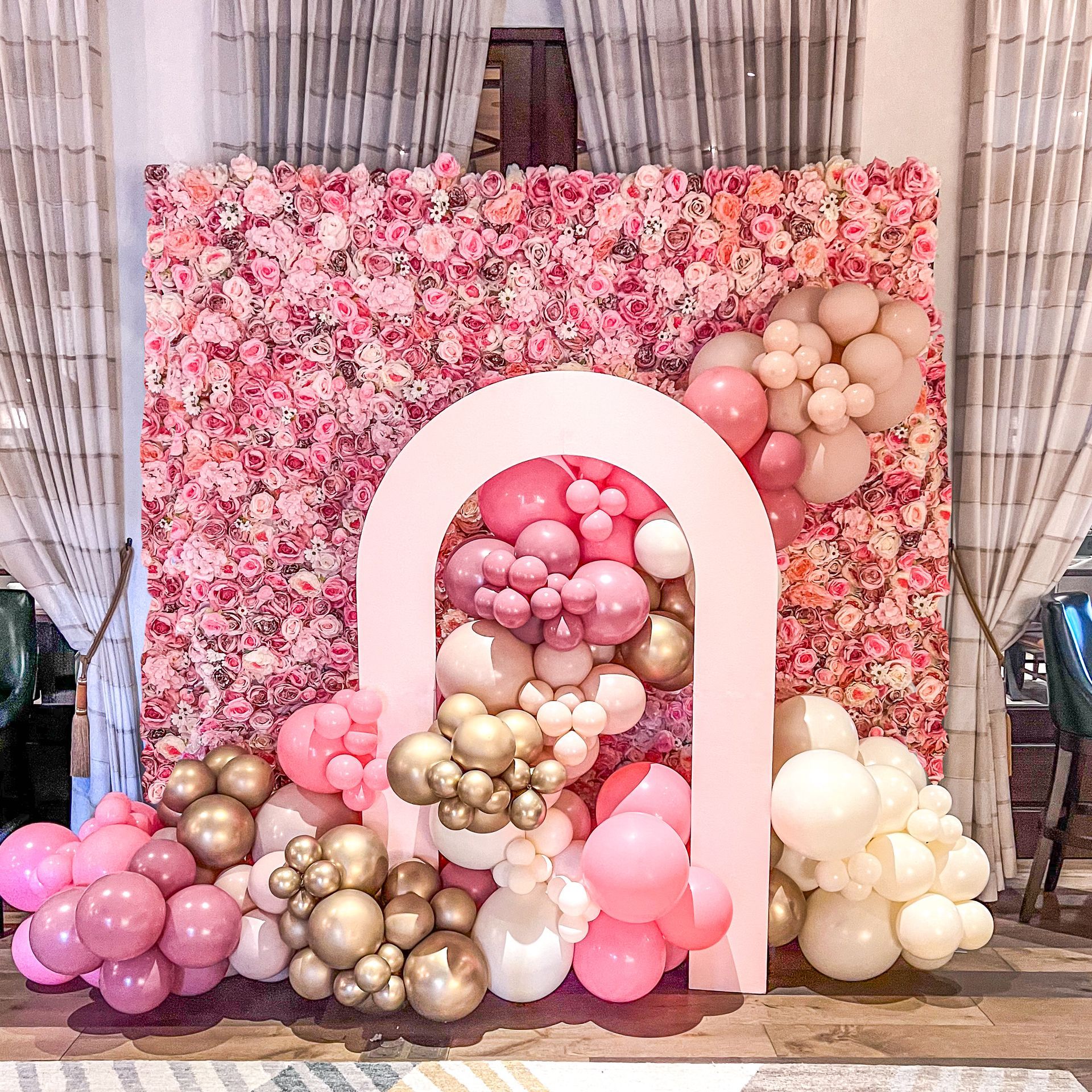 A wall of pink flowers and balloons in a room.