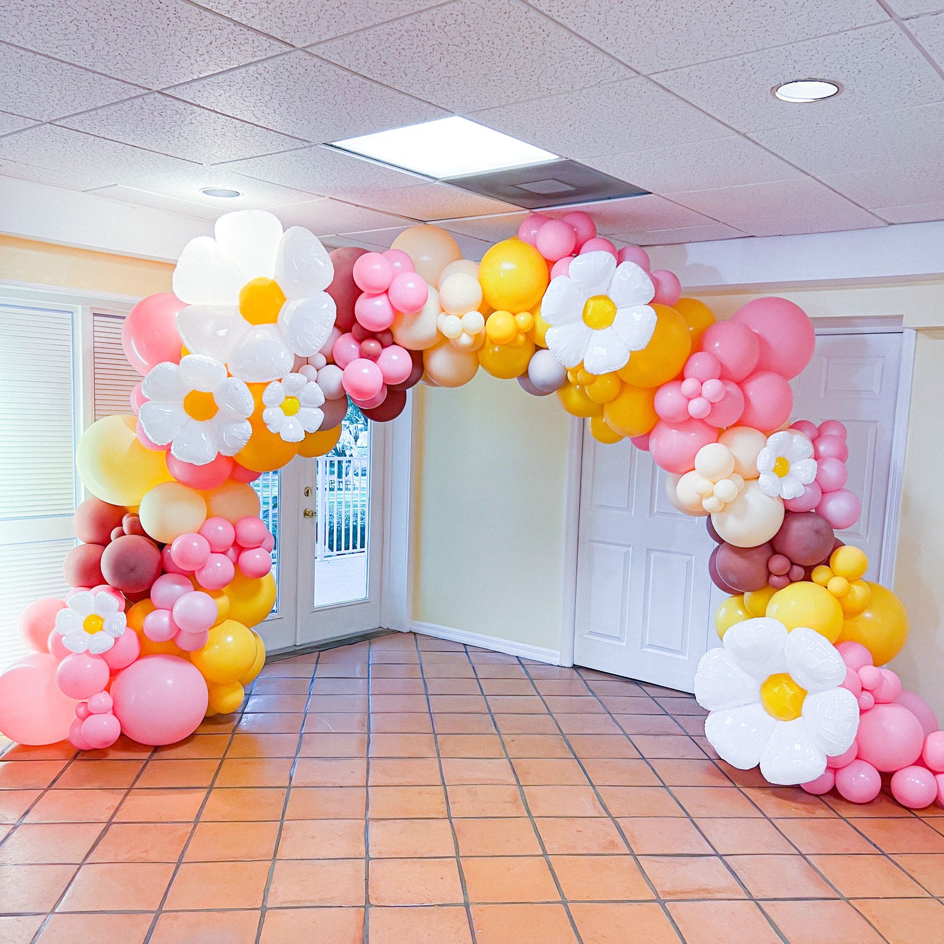 A room decorated with pink , yellow and white balloons and flowers.