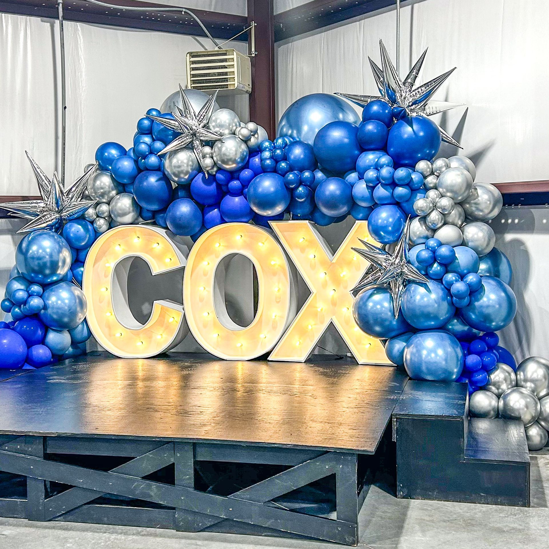A stage decorated with blue and silver balloons and a lighted sign that says cox