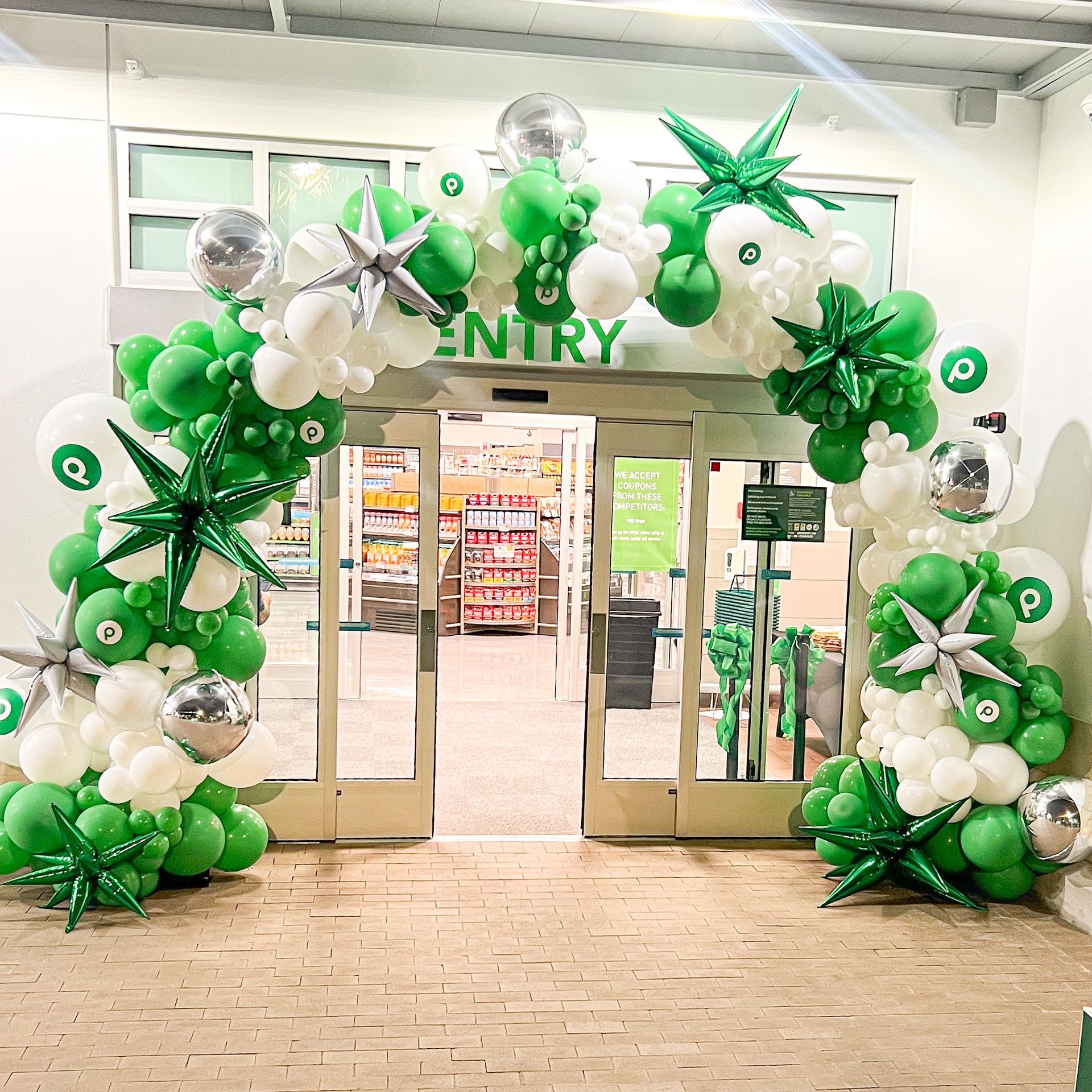 The entrance to a store is decorated with green and white balloons.