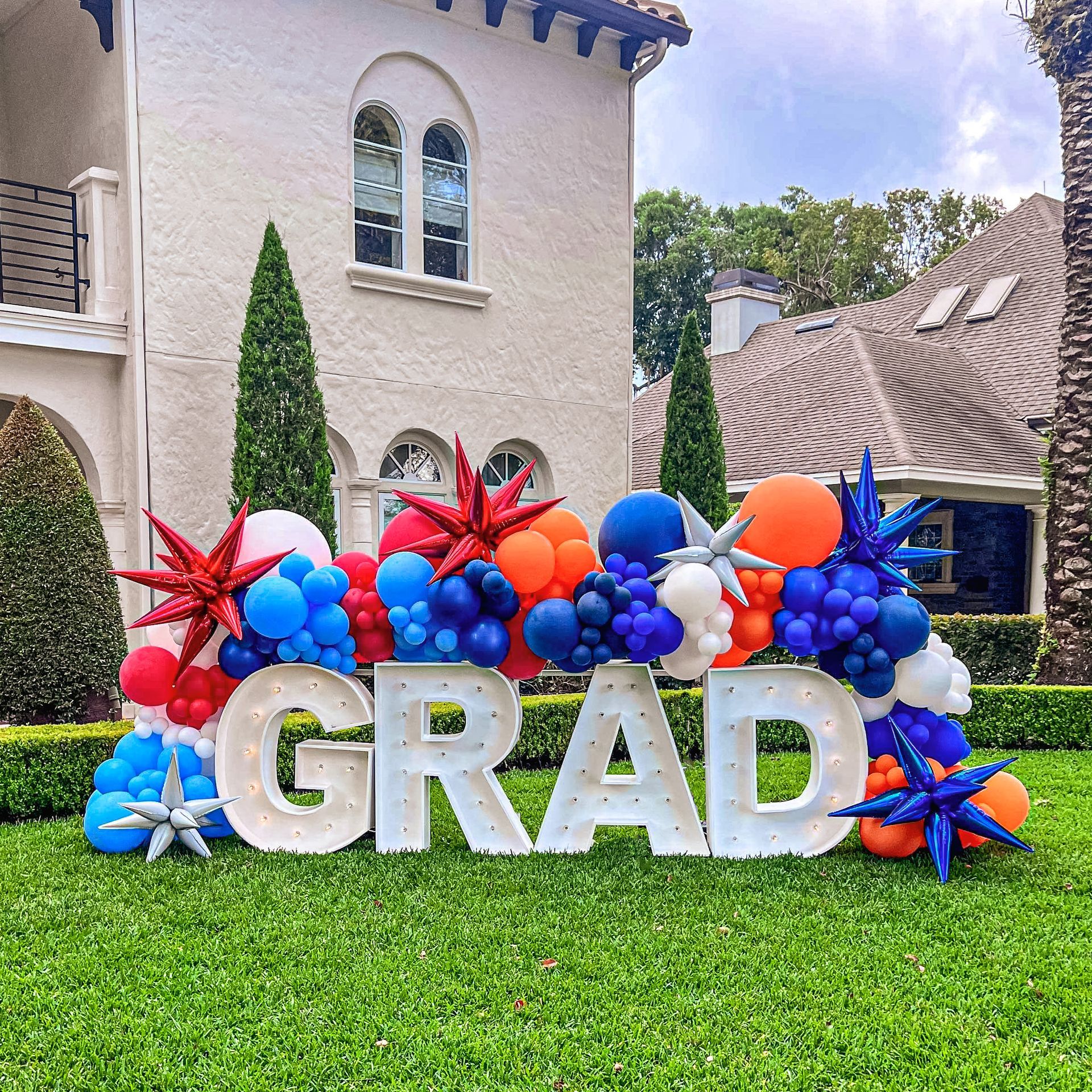 The word grad is surrounded by balloons in front of a house.