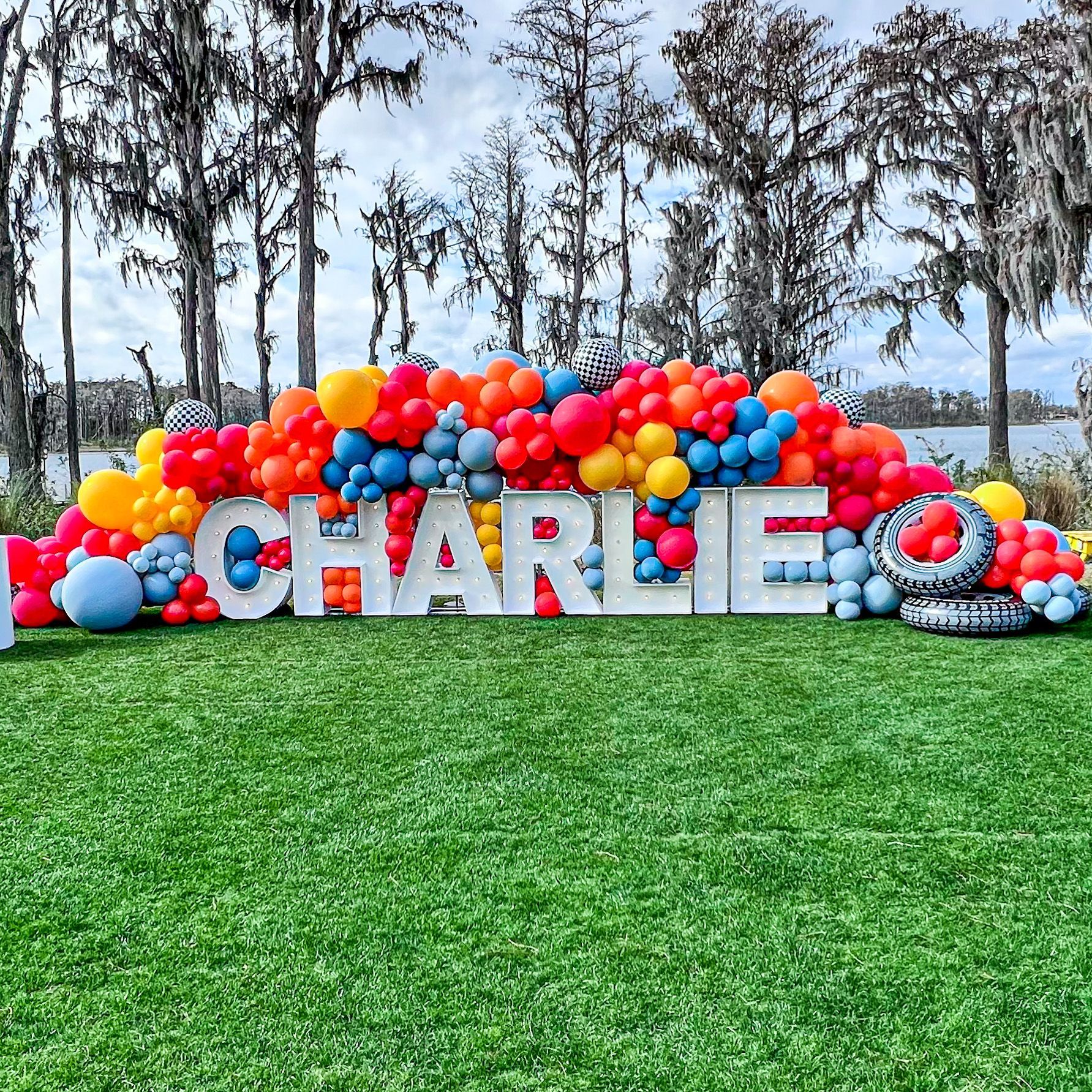 A large sign with the name charlie surrounded by balloons on a lush green field.