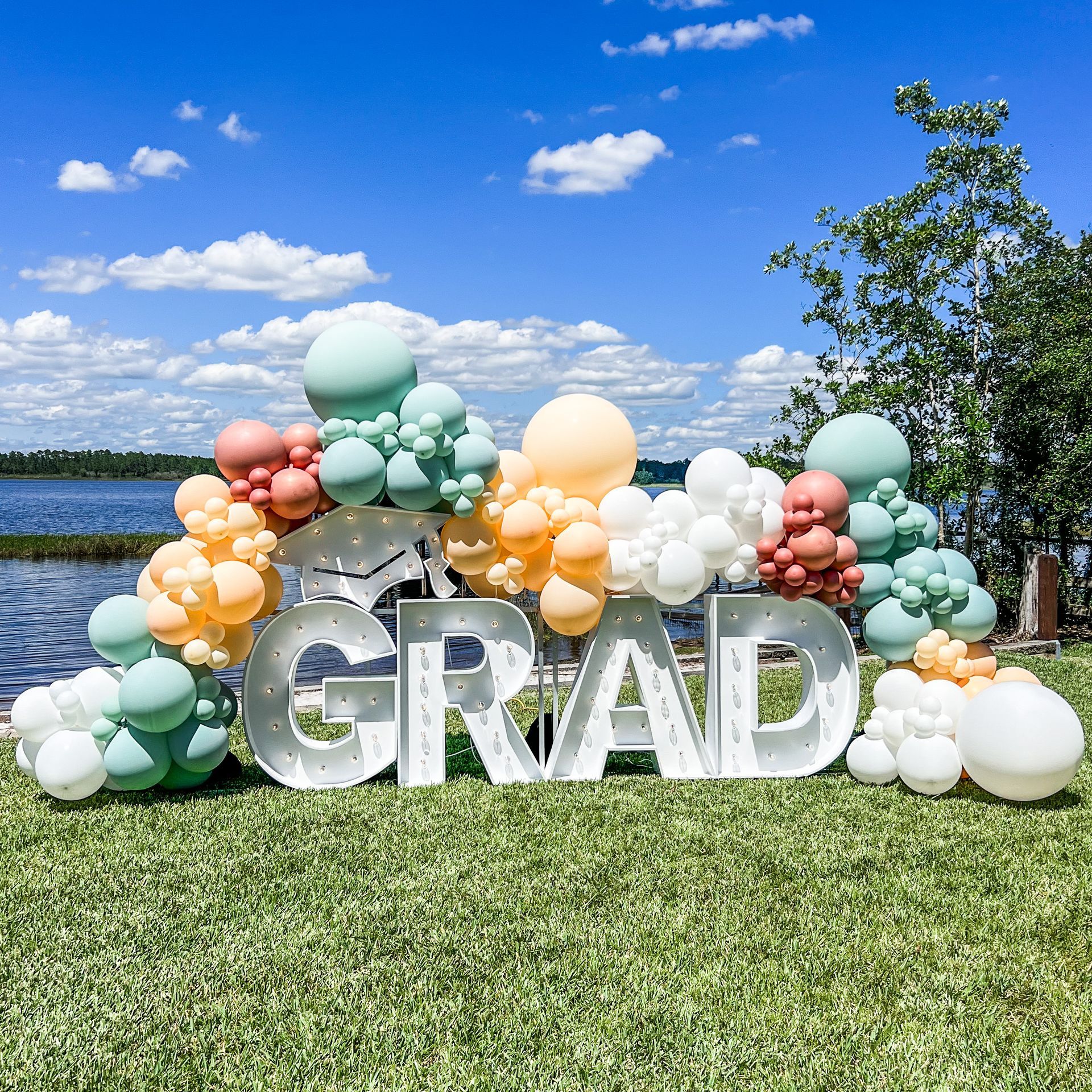 A large sign that says `` grad '' is surrounded by balloons on a lush green field.