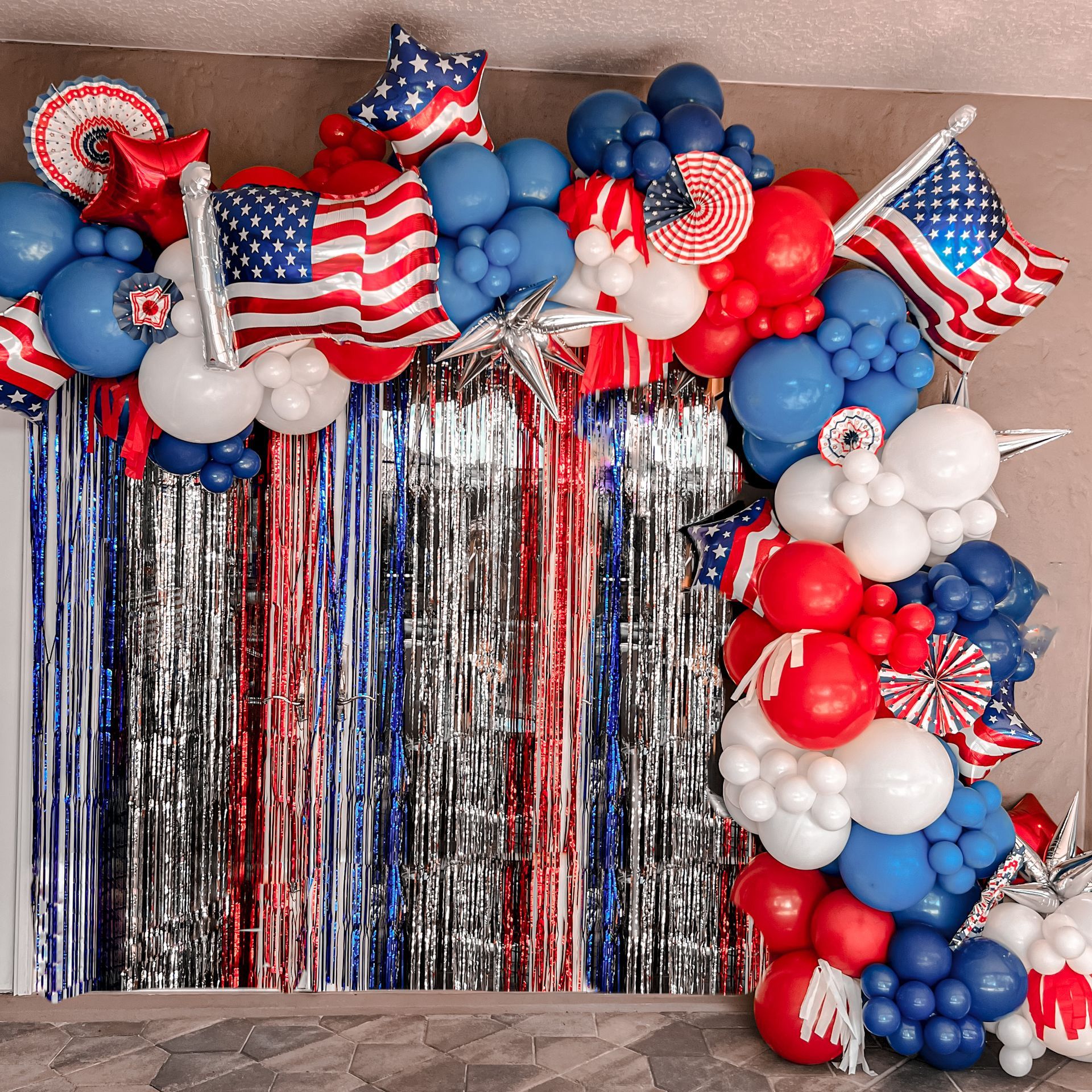 A bunch of red , white and blue balloons are hanging on a wall.