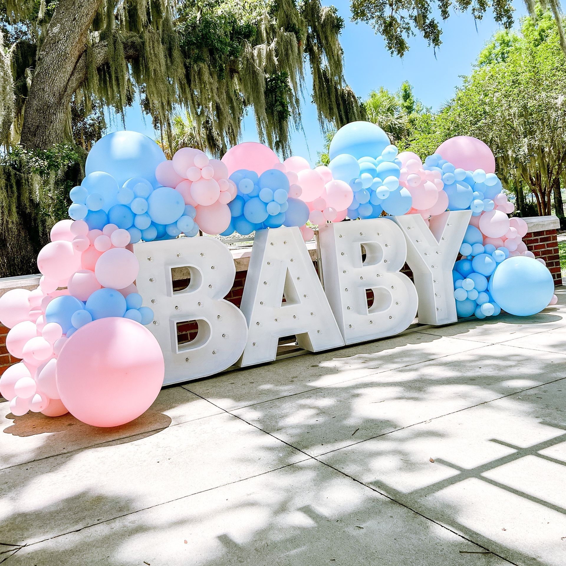 The word baby is surrounded by pink and blue balloons.