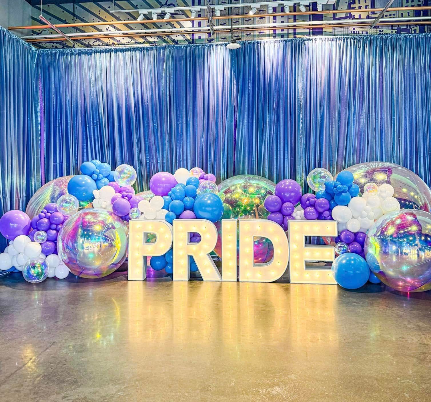 The word pride is surrounded by balloons in a room.