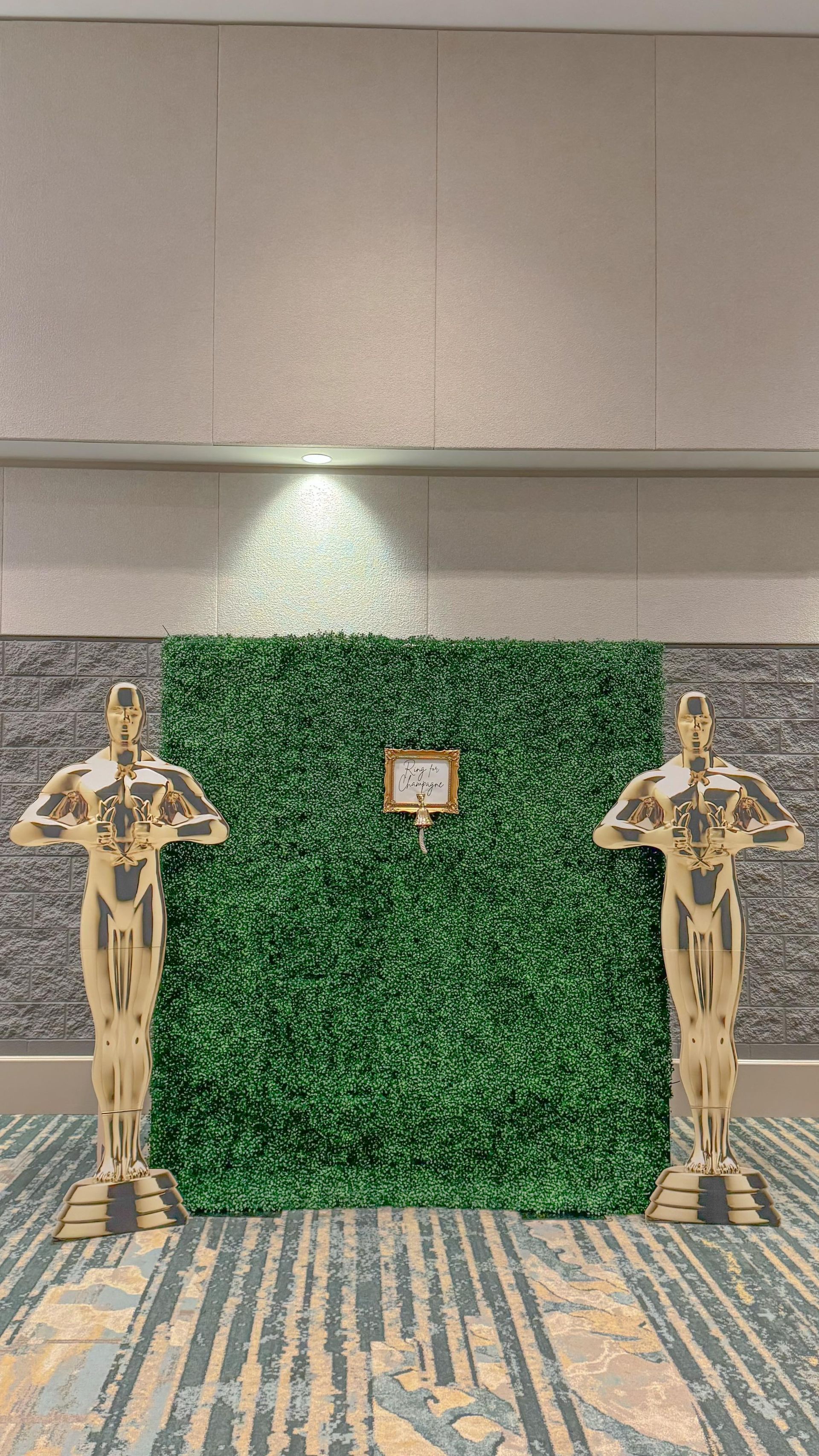 Two oscar statues are standing in front of a green wall that hosts an interactive experience.