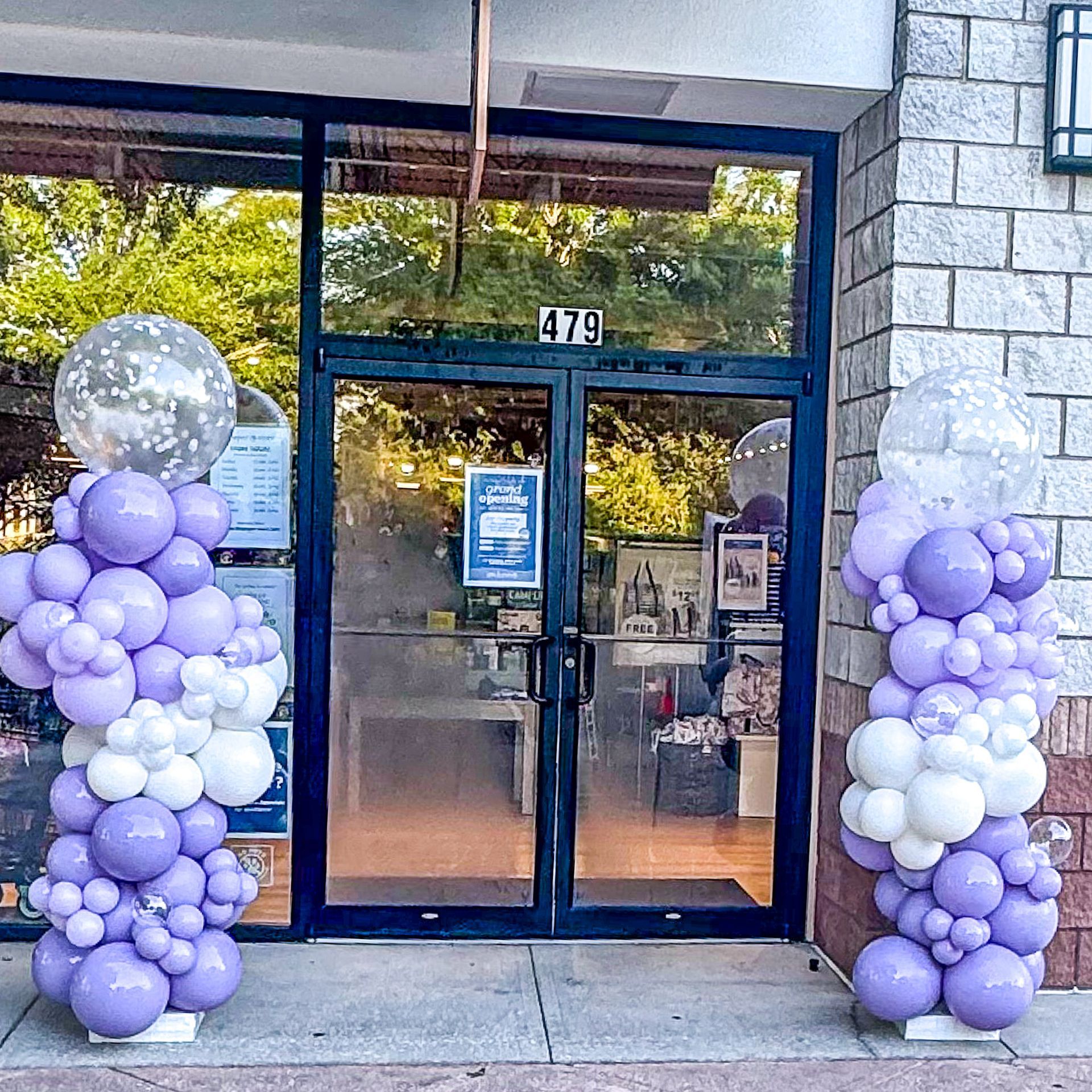 Purple and white balloons are lined up in front of a store door.