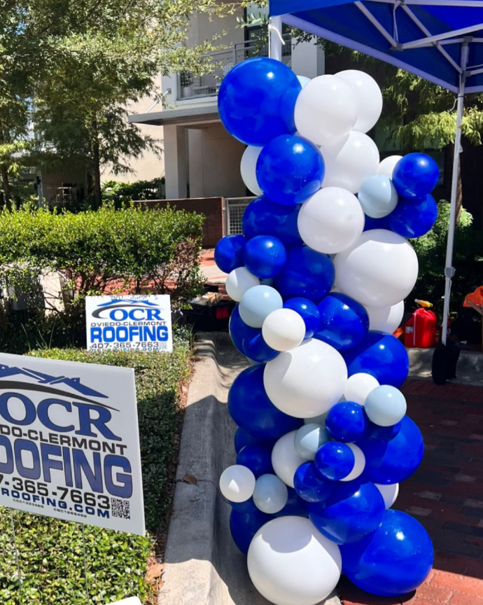 A sign for ocr roofing is surrounded by blue and white balloons