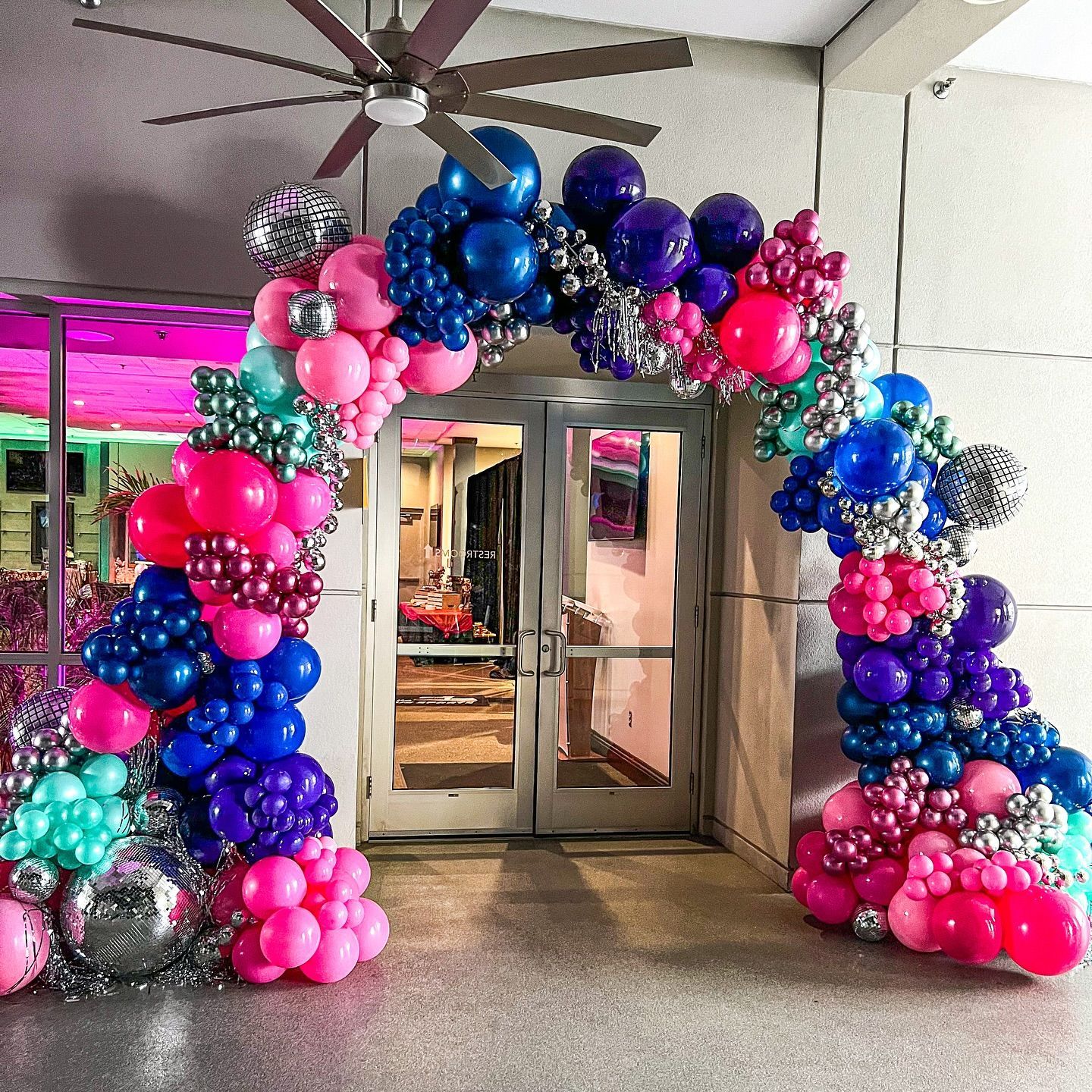 A large arch made of colorful balloons is in front of a door.
