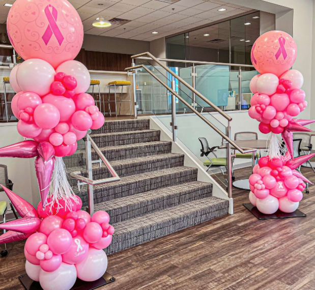 Two pink ribbon balloon sculptures by stairs for breast cancer awareness.