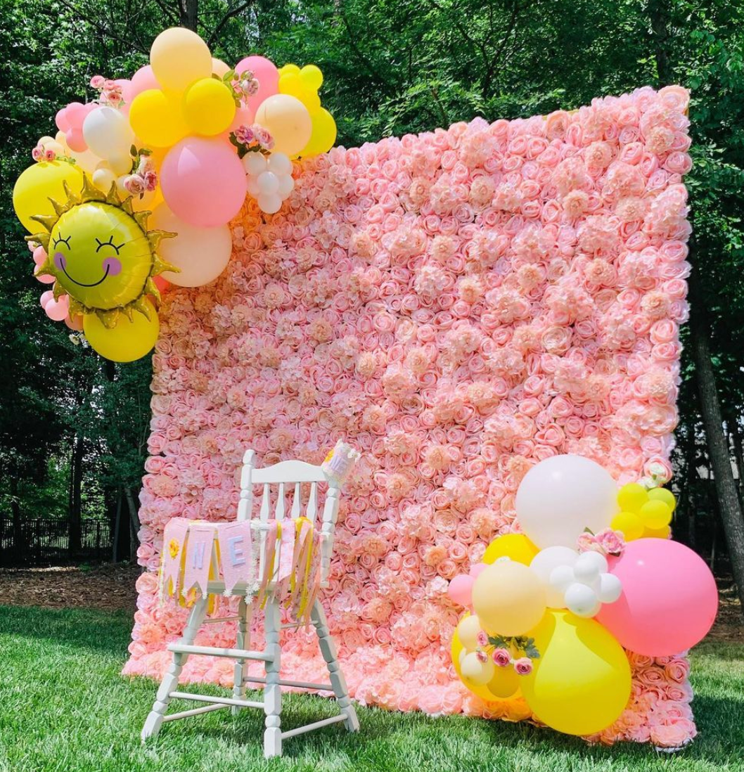 a pink flower wall with balloons and a chair in front of it .