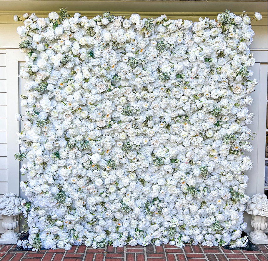 A wall of white flowers is sitting on a brick floor.