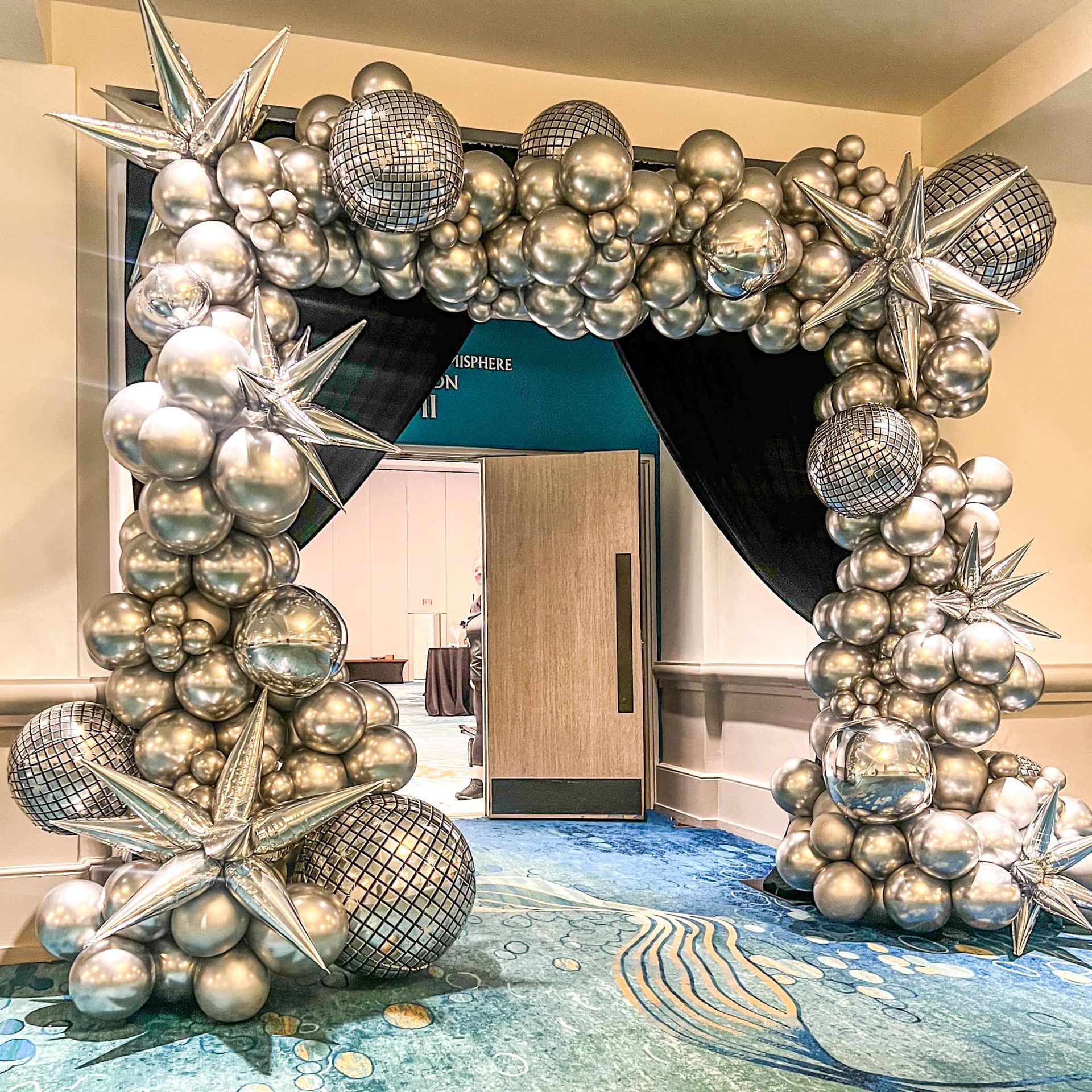 Silver balloon arch with disco balls and starburst accents framing a doorway.