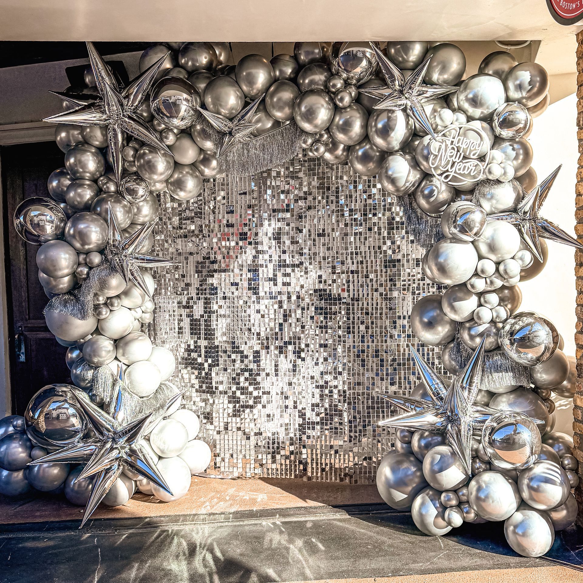 Silver balloon arch with star accents frames a mirrored backdrop.