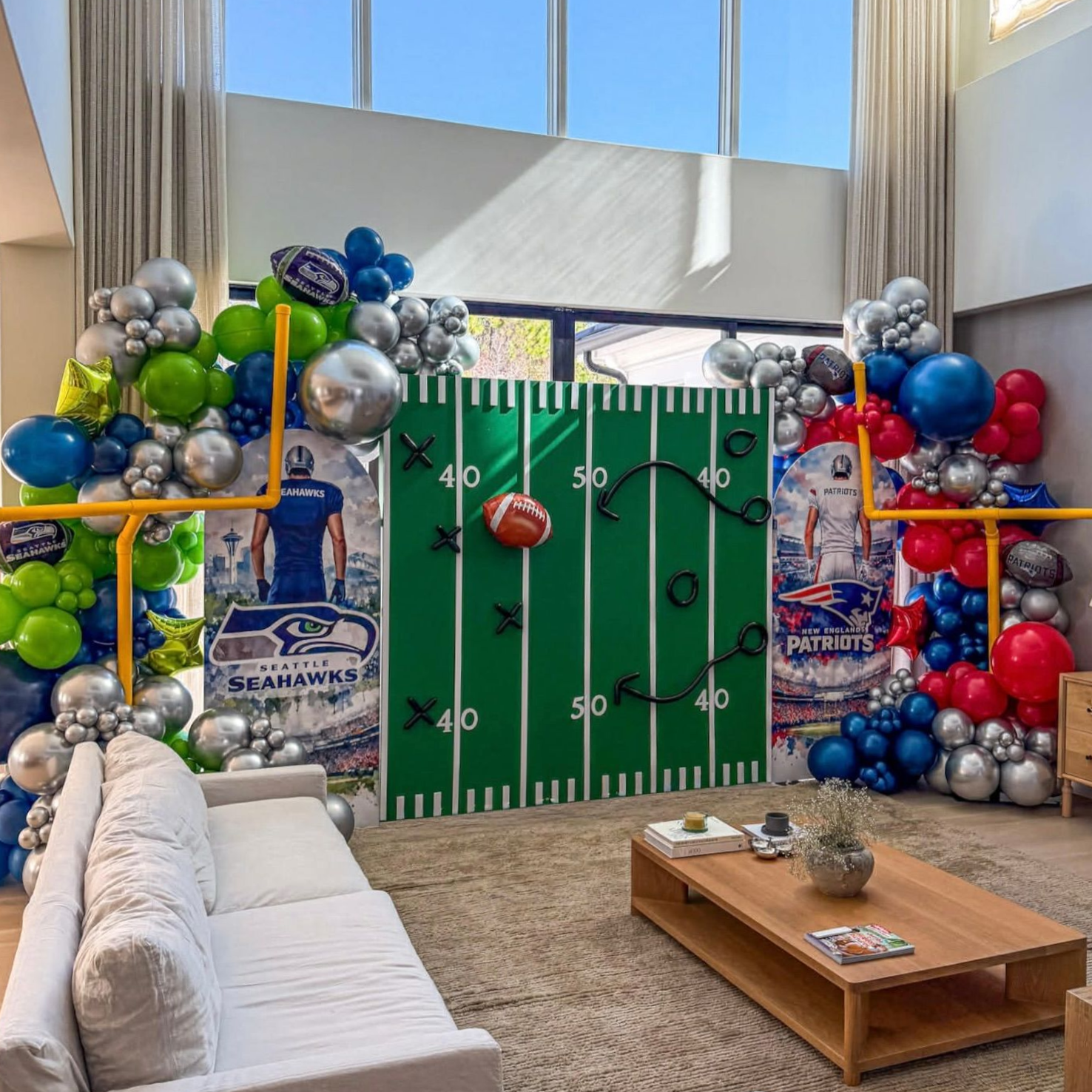 Living room decorated for a football party with balloon arches, a field backdrop, and team banners.