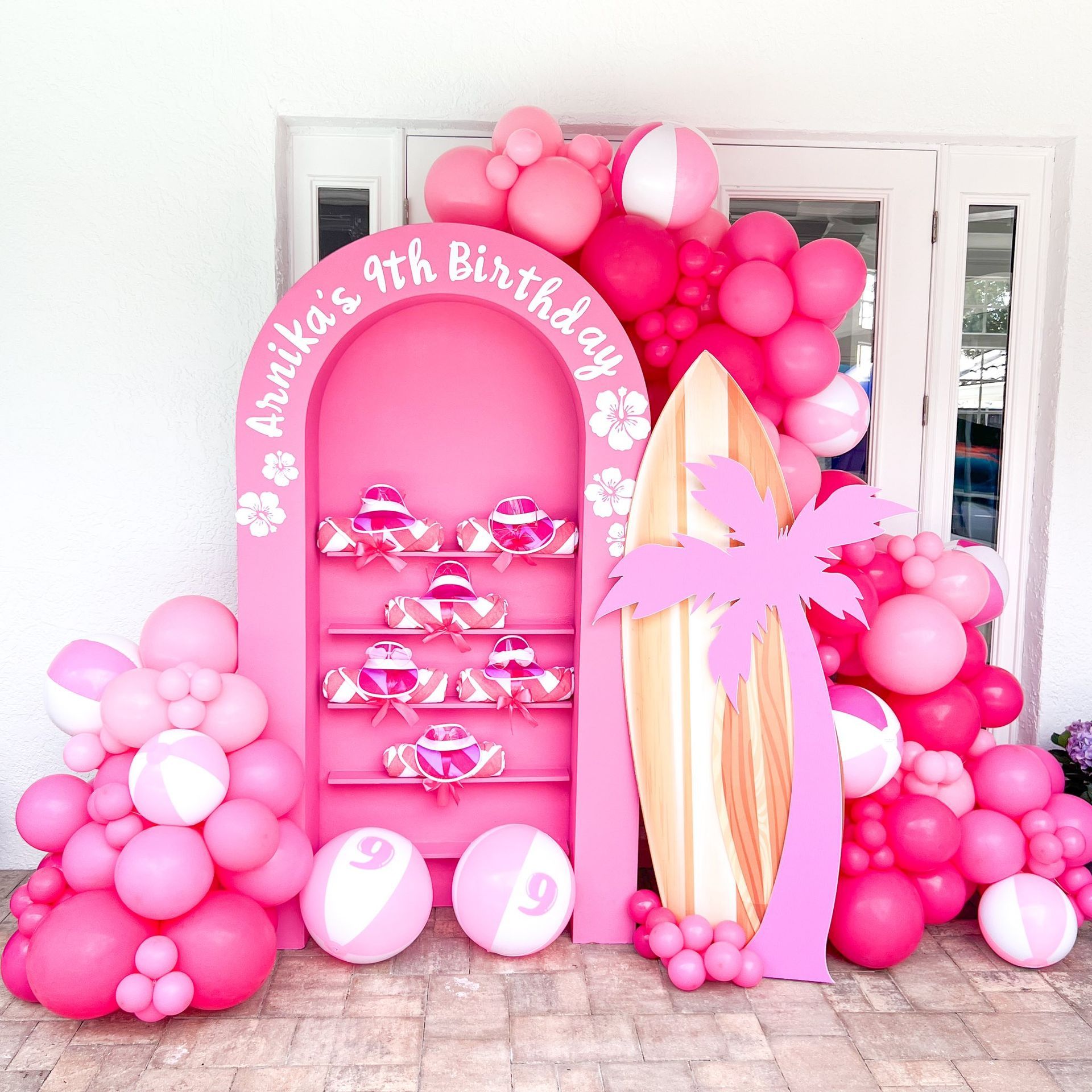 A pink display with balloons and a surfboard for a girl 's 9th birthday.