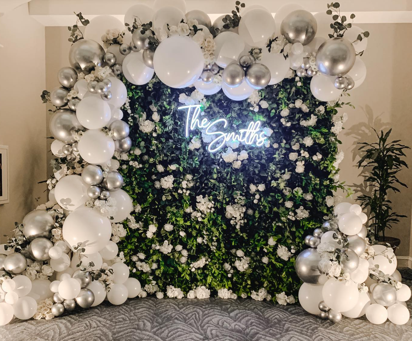 a wall of balloons and flowers with a neon sign that says the smiths .