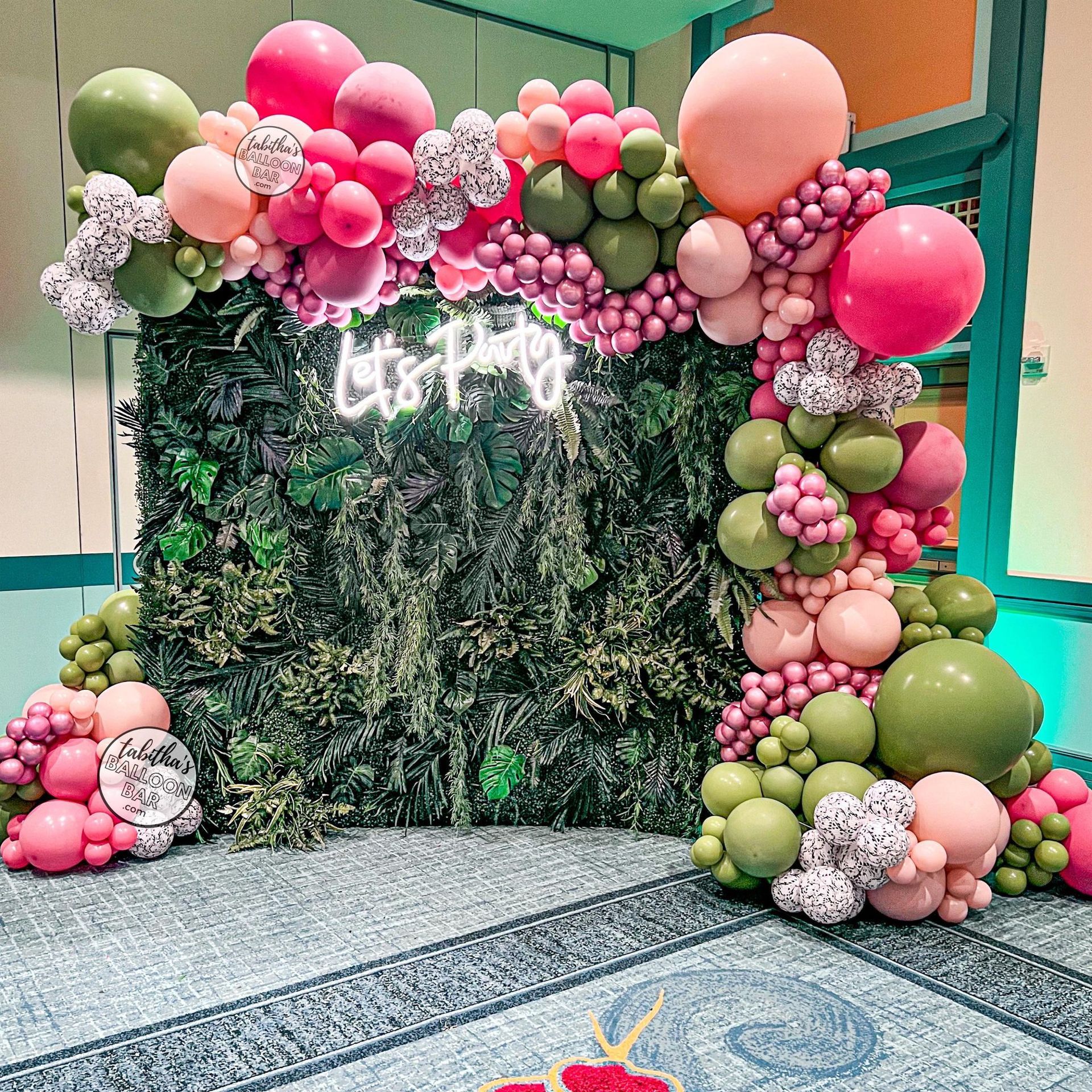a wall covered in pink and green balloons and a neon sign .