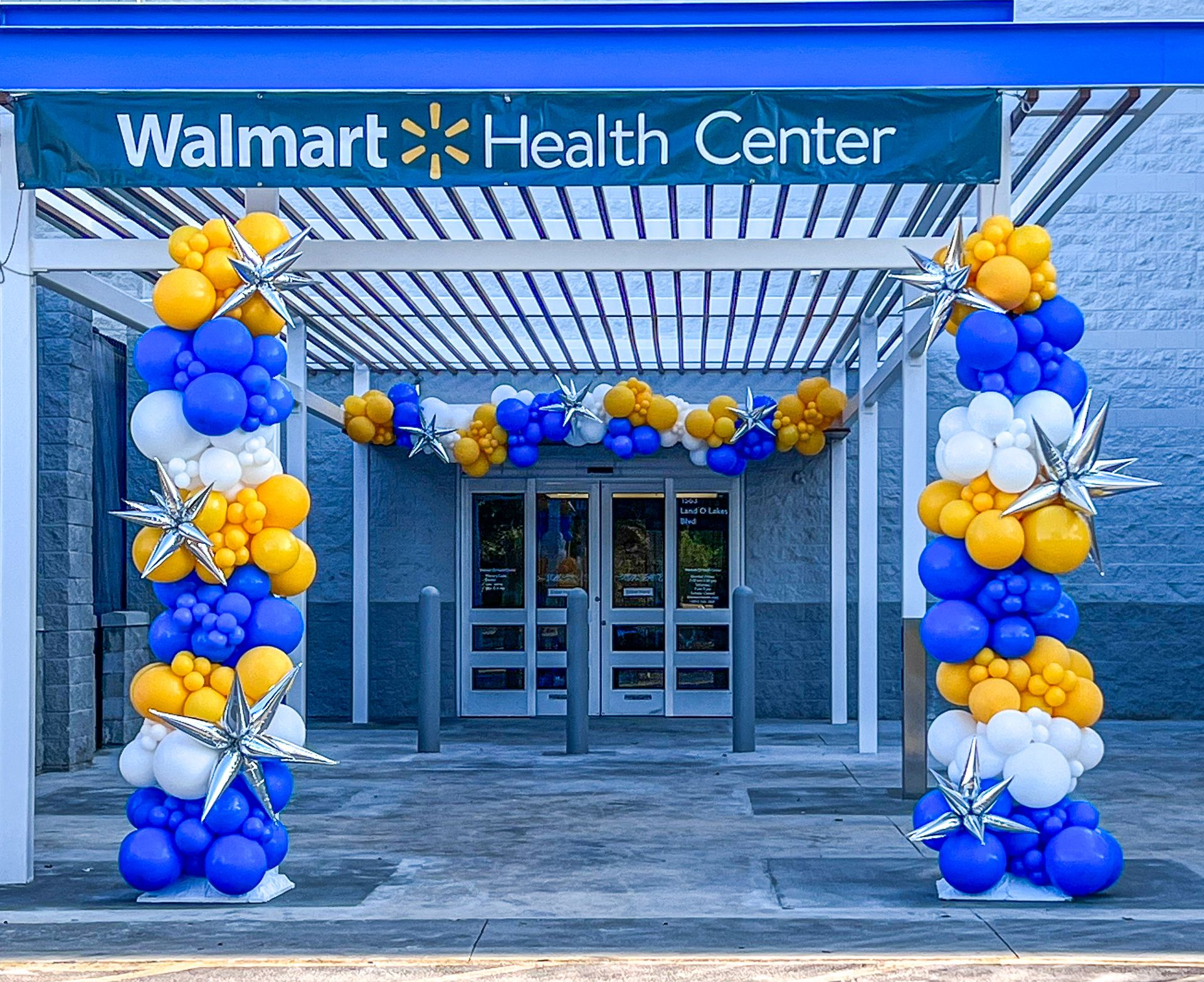 Walmart Health Center entrance decorated with blue, yellow, and white balloons and silver star accents.