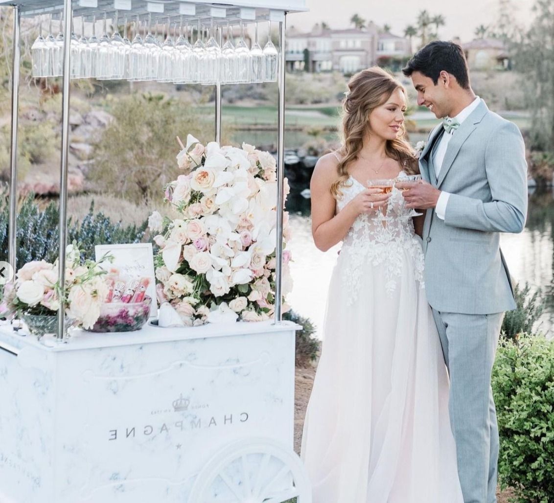 a bride and groom are standing next to a drink cart .