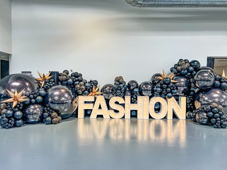 The word fashion is surrounded by balloons in a room.