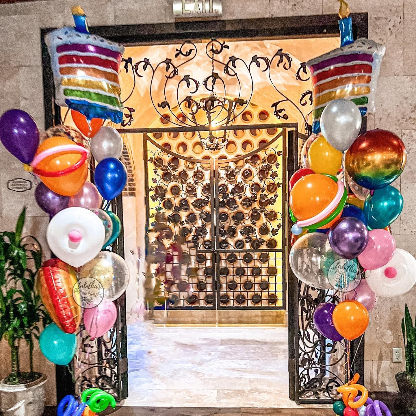 A bunch of balloons are hanging from a gate in a room.