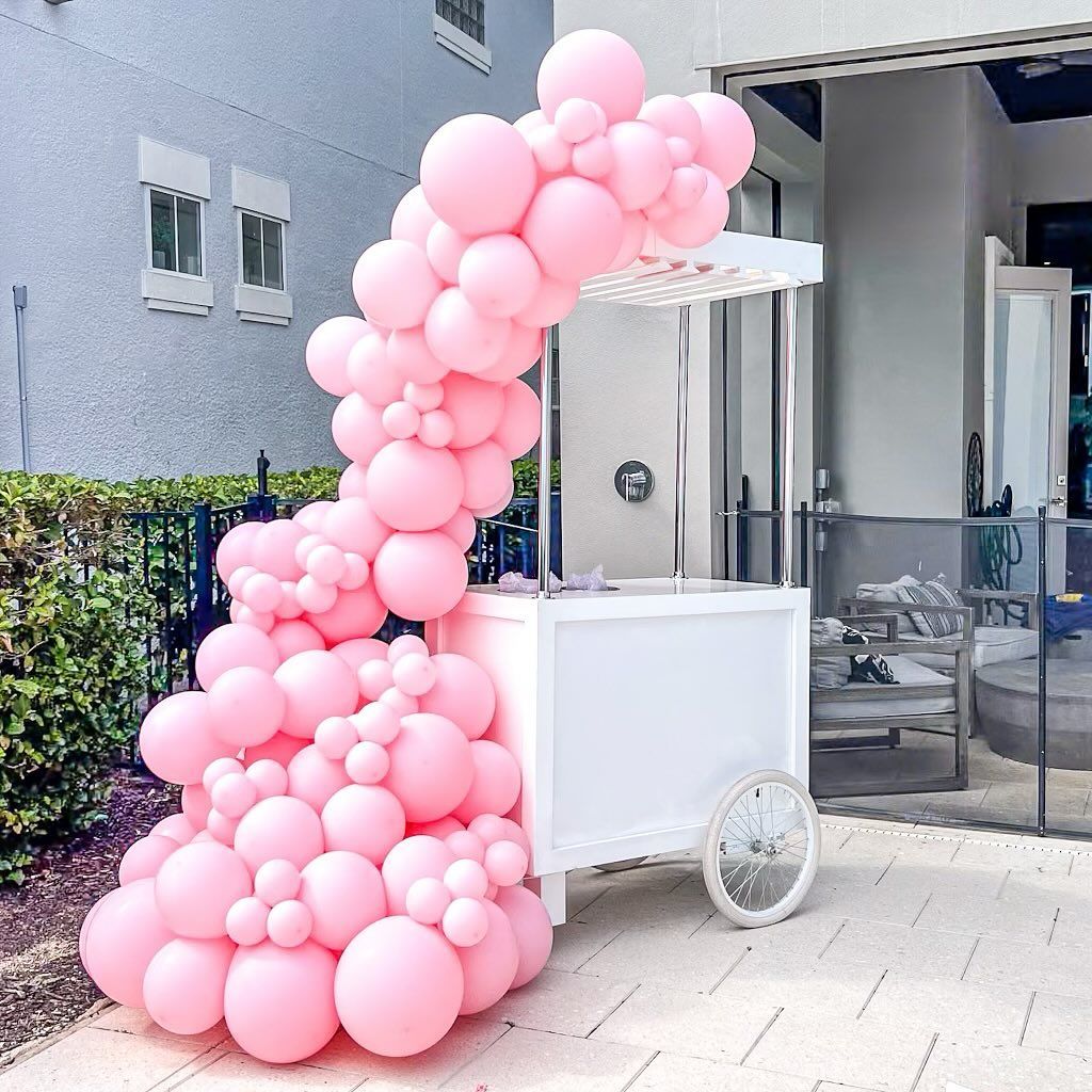 A white cart is decorated with pink balloons.