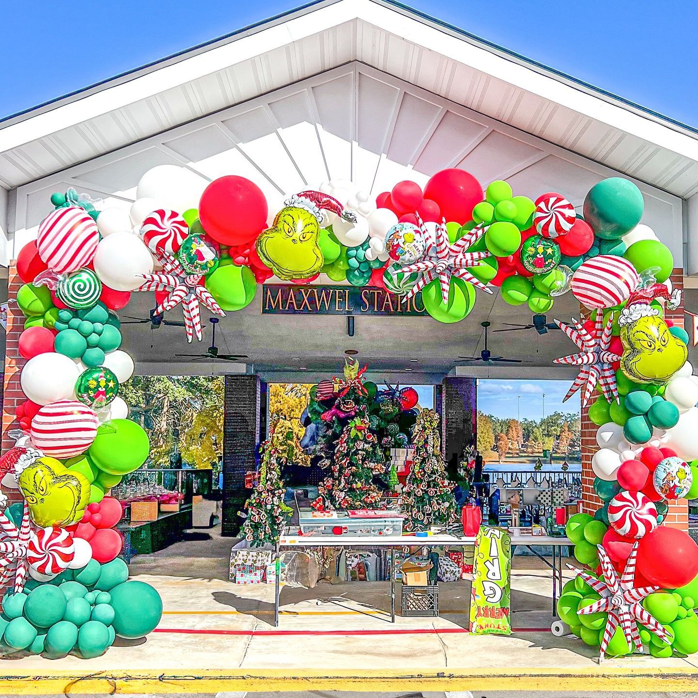 Christmas-themed archway with red, green, and white balloons, Grinch, and candy cane decorations, over a Christmas tree display.