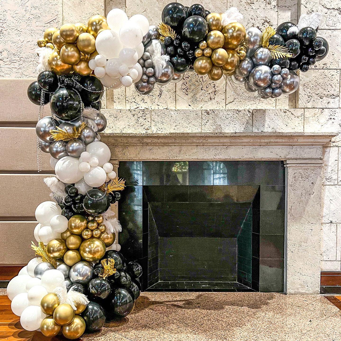 A fireplace decorated with black , white and gold balloons.