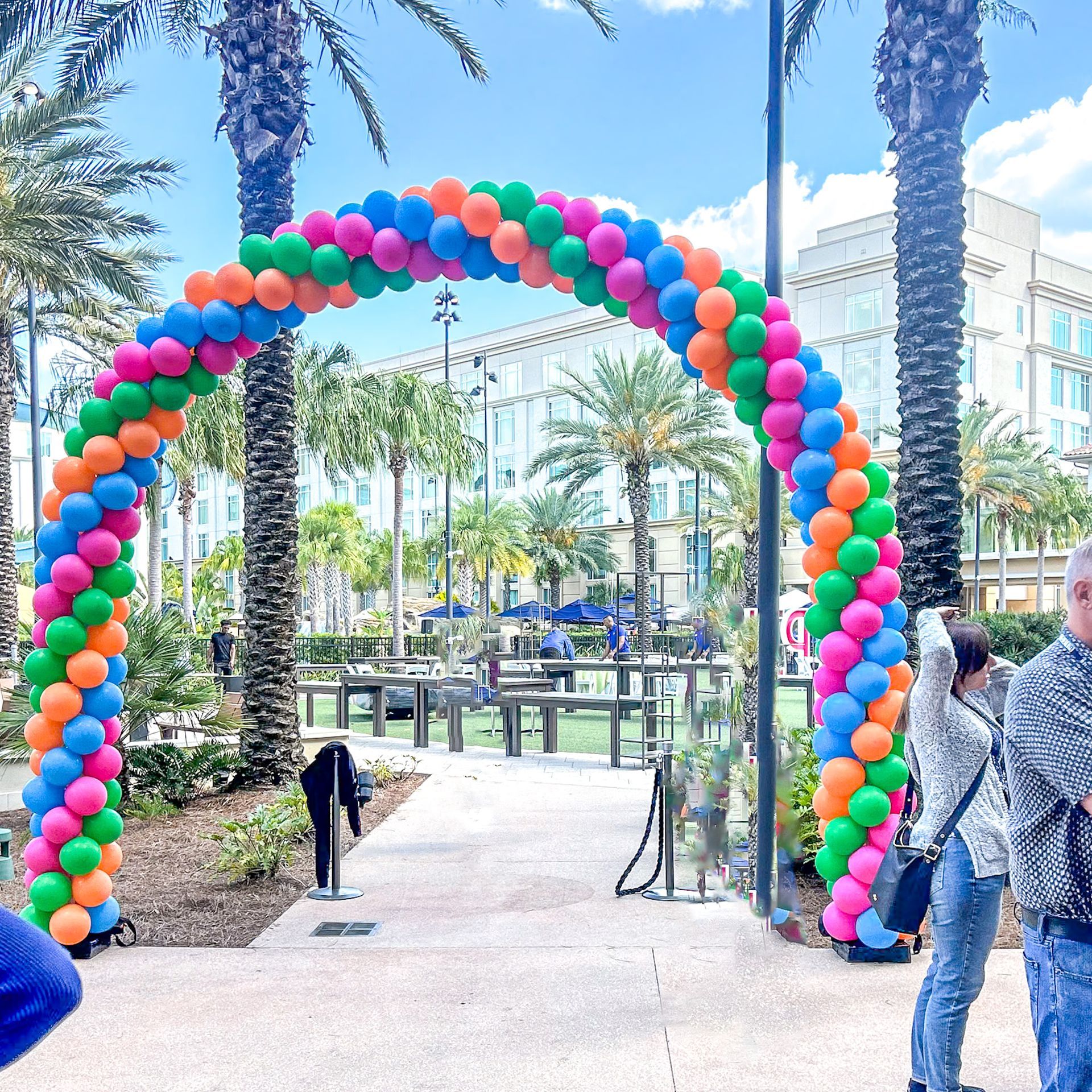 A colorful balloon arch is surrounded by palm trees