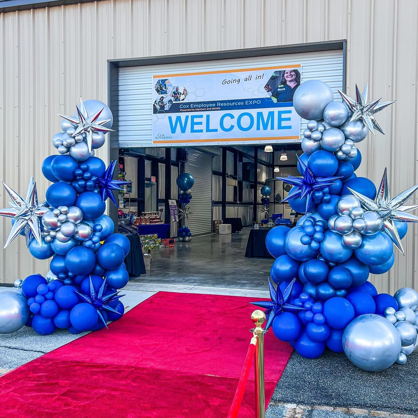 A red carpet is lined up in front of a building with balloons and a welcome sign.