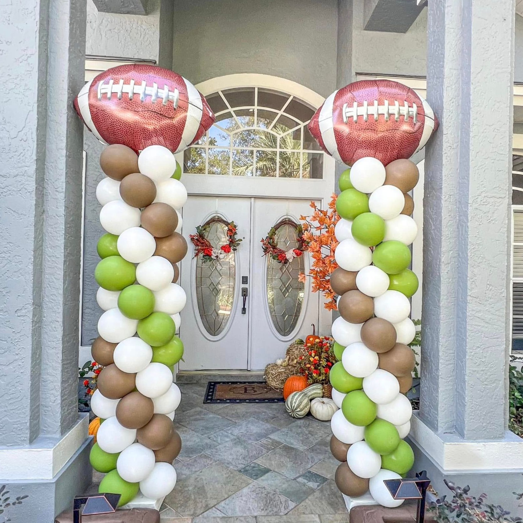 Two balloon columns flank a door decorated for fall, topped with football balloons.