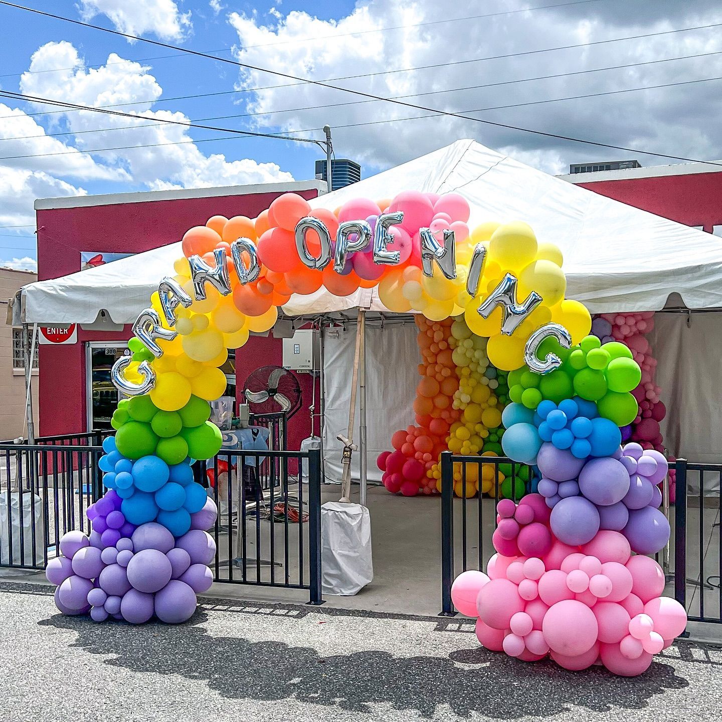 A rainbow colored balloon arch with the words grand opening written on it