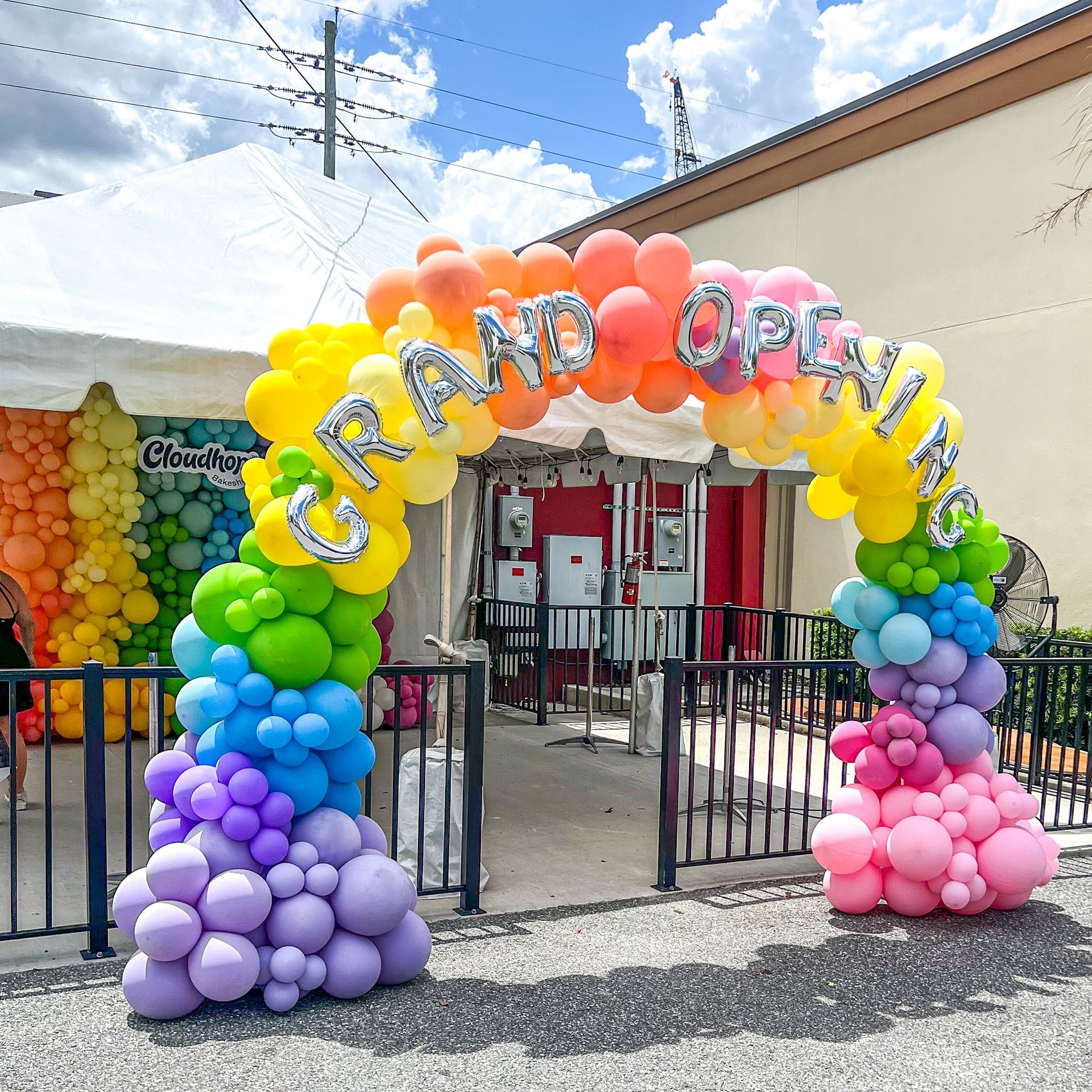 A rainbow colored balloon arch with the words grand opening written on it