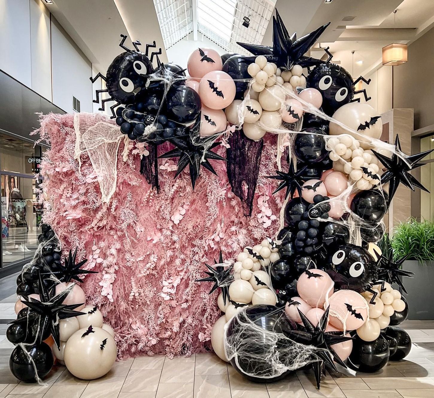 a wall covered in balloons and flowers in a mall .